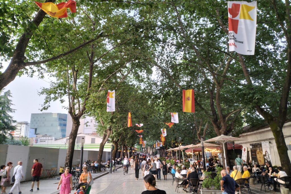 A busy pedestrian street in Tirana lined with cafes and trees