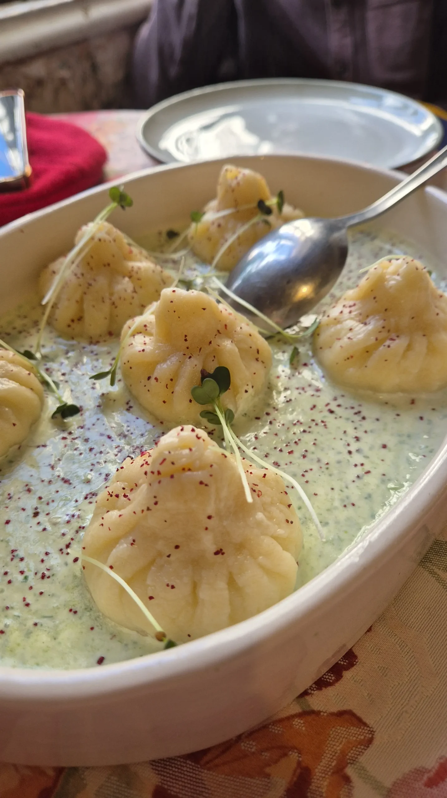 Cheesy saucy khinkali a bowl of a creamy herby sauce topped with small khinkali (Georgian dumplings filled with cheese) and topped with pink sumac and cress from Cafe Linville, Tbilisi