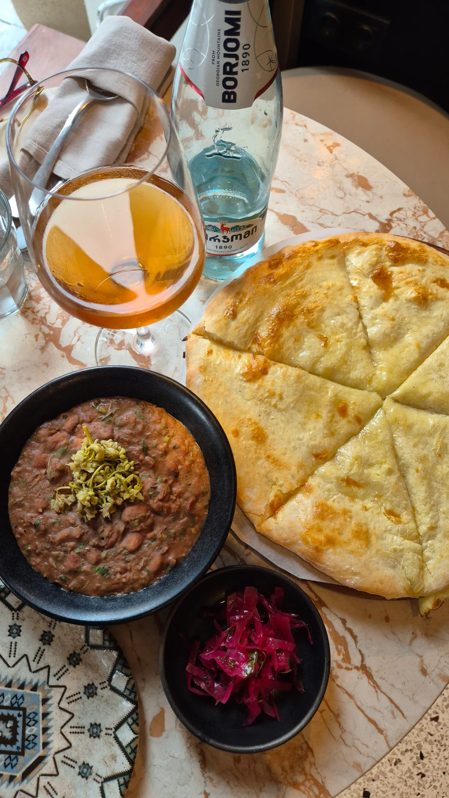 Lobio with jonjoli, Imeretian khachapuri cheese bread, Borjomi water, and a glass of amber wine - Georgian meal at Pkhali Khinkali, Tbilisi