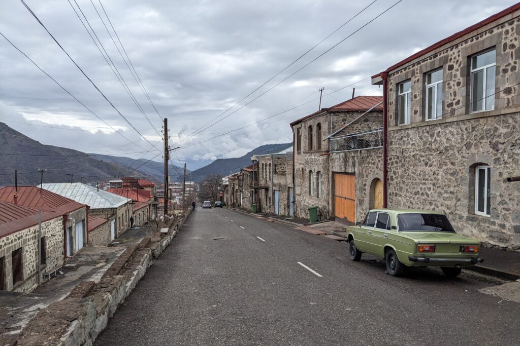 armenian street with green Lada parked up and mountains in the background, how to get to tatev