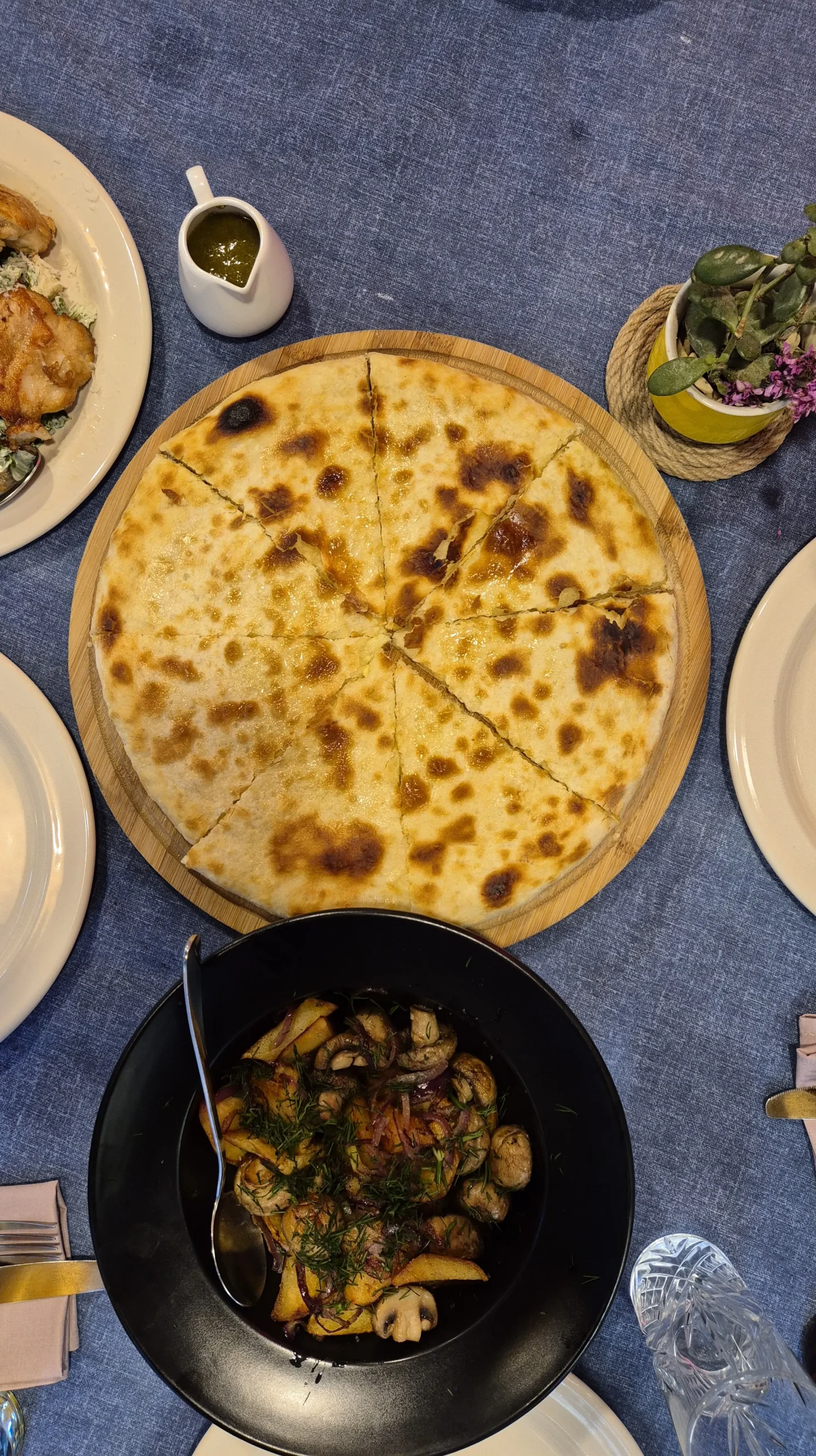 palaty kutaisi an Imereitian khachapuri sits on a wooden board next to a bowl of mushrooms and potaotes with herbs
