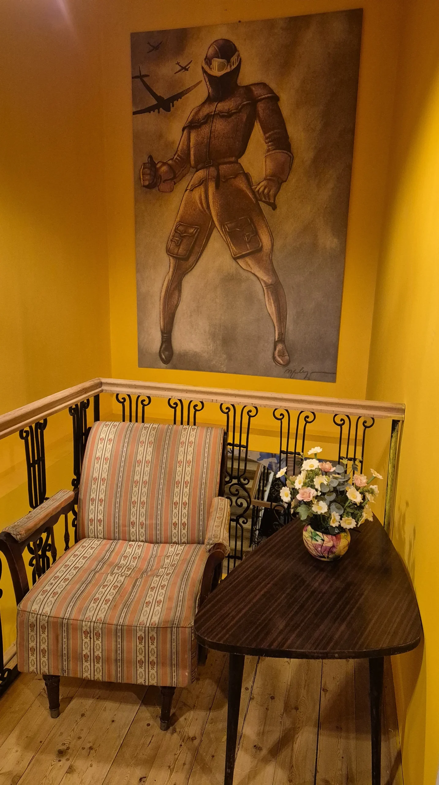 Teahouse Foe Foe an arm chair has a wooden table next to it. the walls are yellow and have a large painting of a pilot