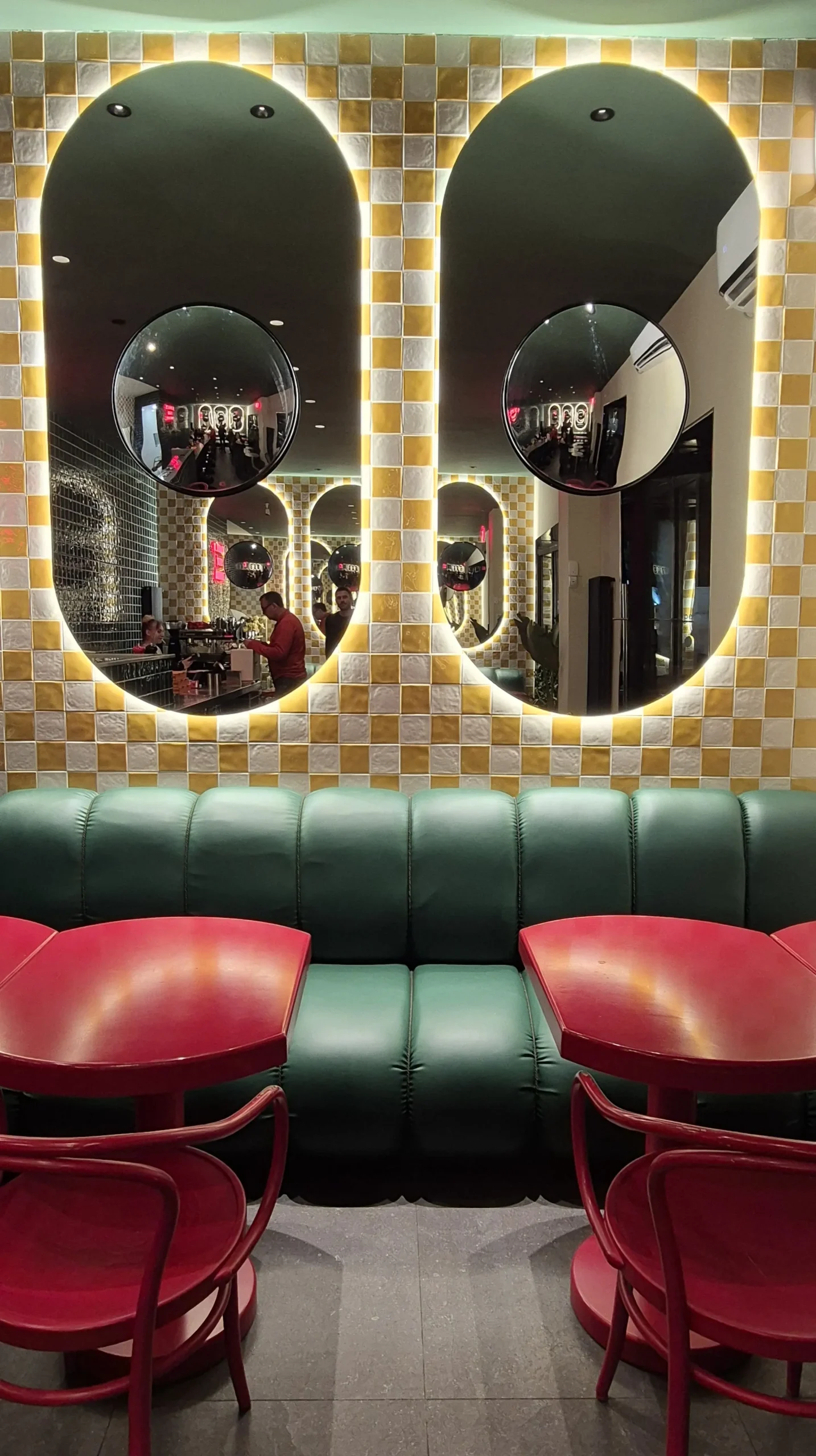 story kutaisi a yellow and white tiled wall has two large oval shaped mirrors on it and a green sofa with red dining tables in front of it in Pizzeria Dolce, Kutaisi, Georgia