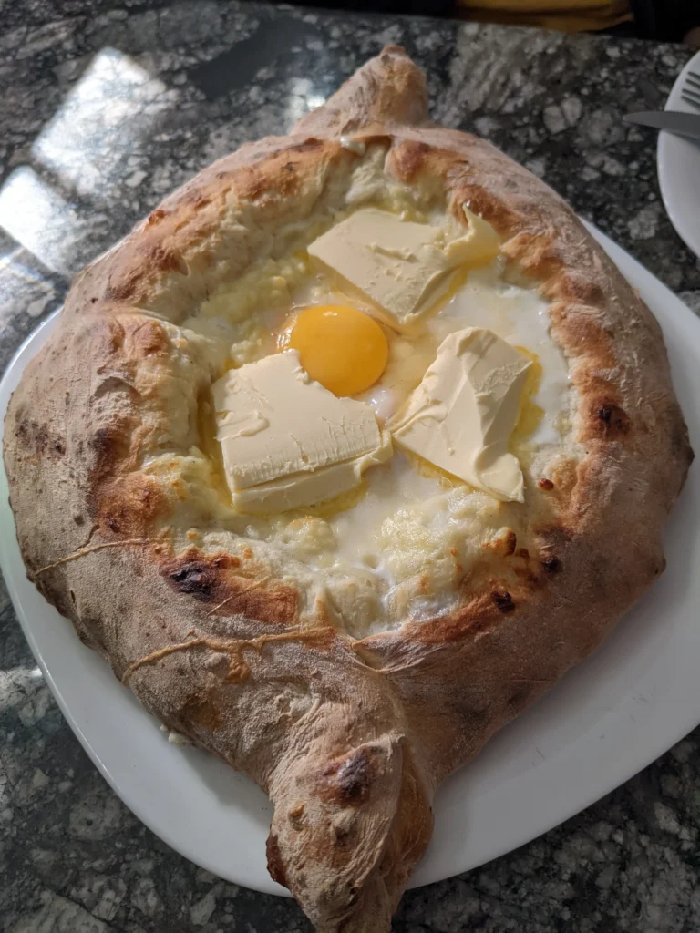 an Adjarian khachapuri is a large bread boat filled with melted cheese, topped with a runny egg yolk and slabs of butter