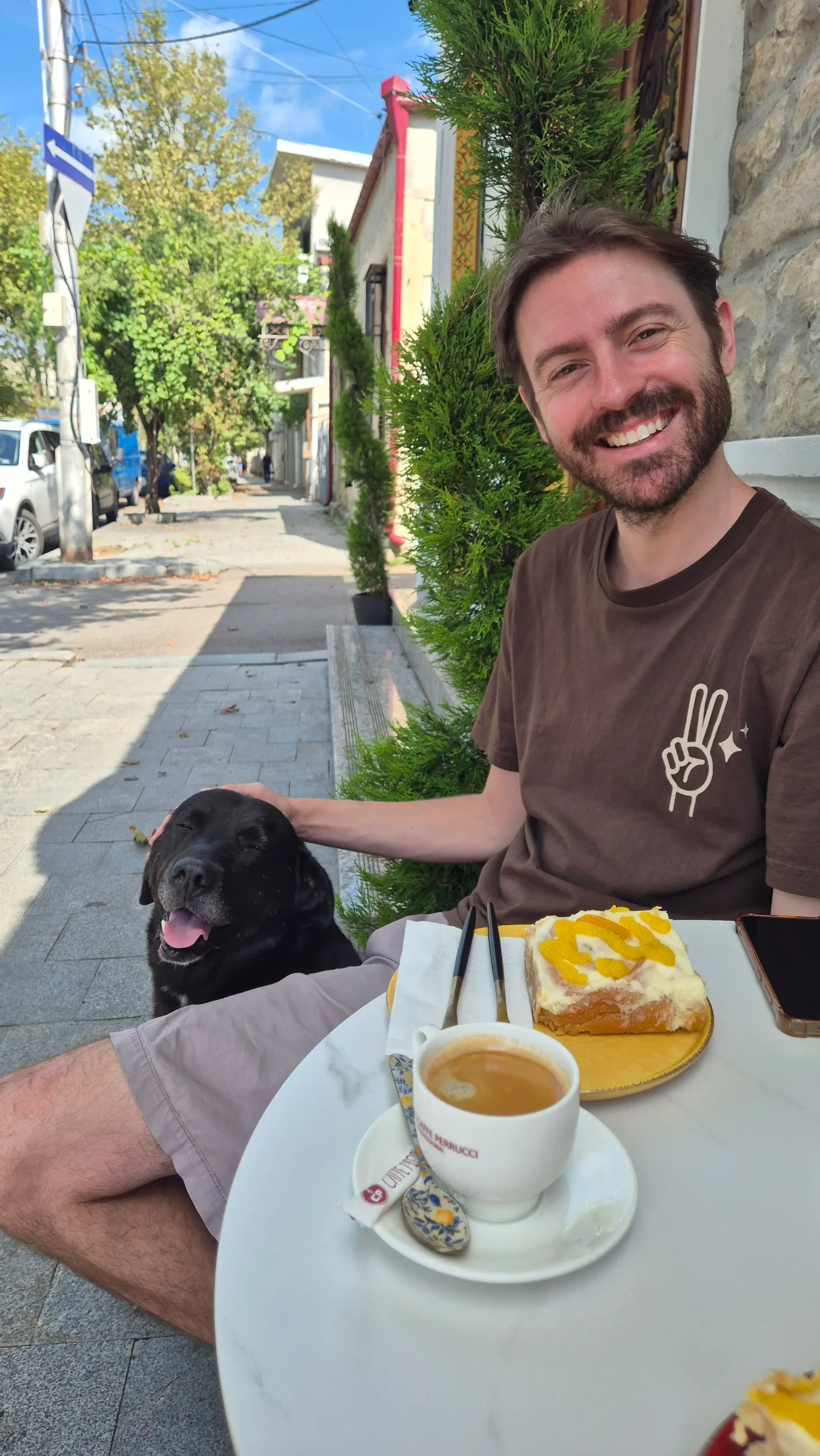 Cinnelle Kutaisi a man sits at a cafe with a coffee and pastry while a dog sits beside him at Cinnelle, Kutaisi