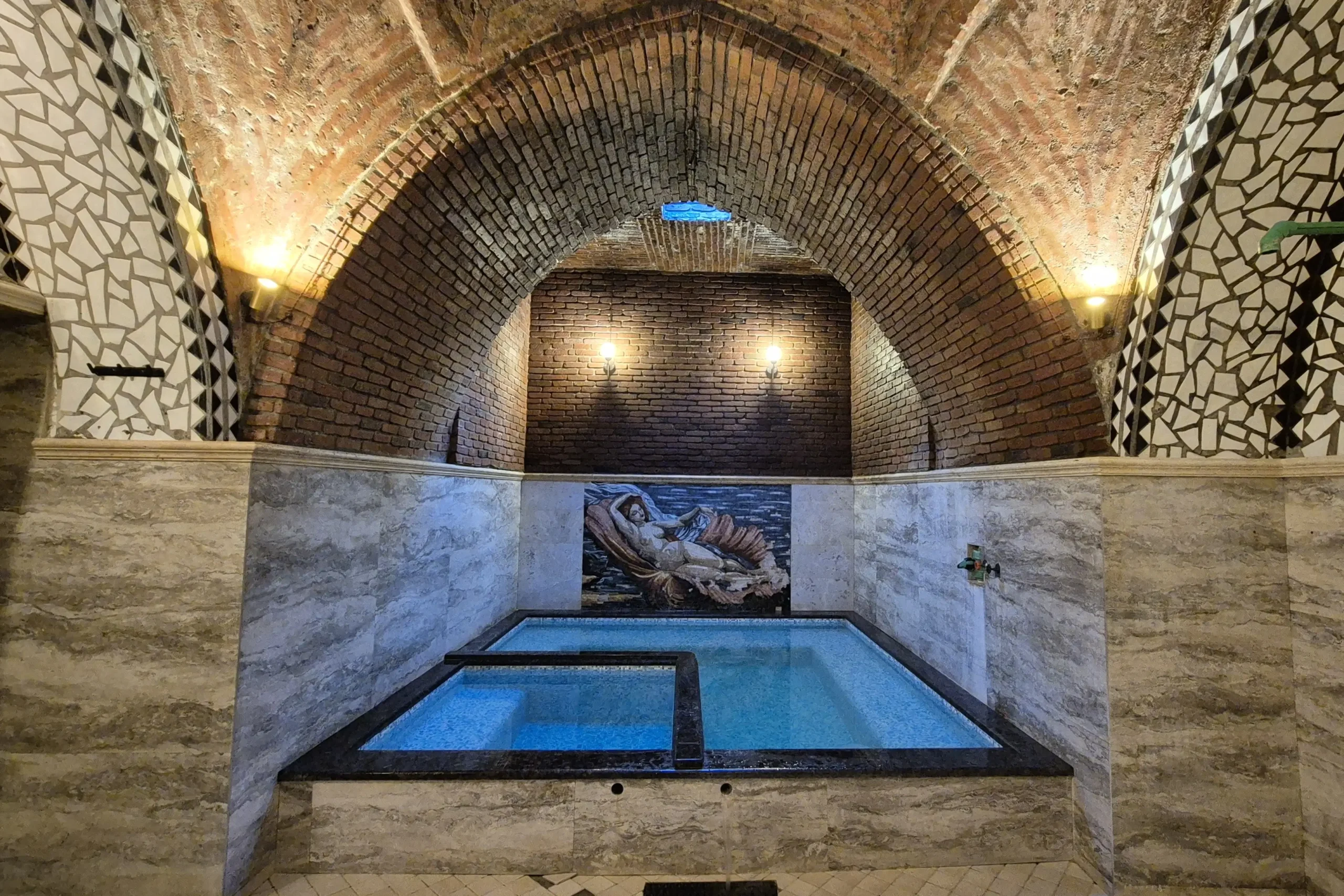 Tbilisi Sulphur Bath a room with a domed brick ceiling and has pool in the centre, atmospheric lighting and a mosaic on the wall at Gulo's Thermal Spa, Tbilisi, Georgia