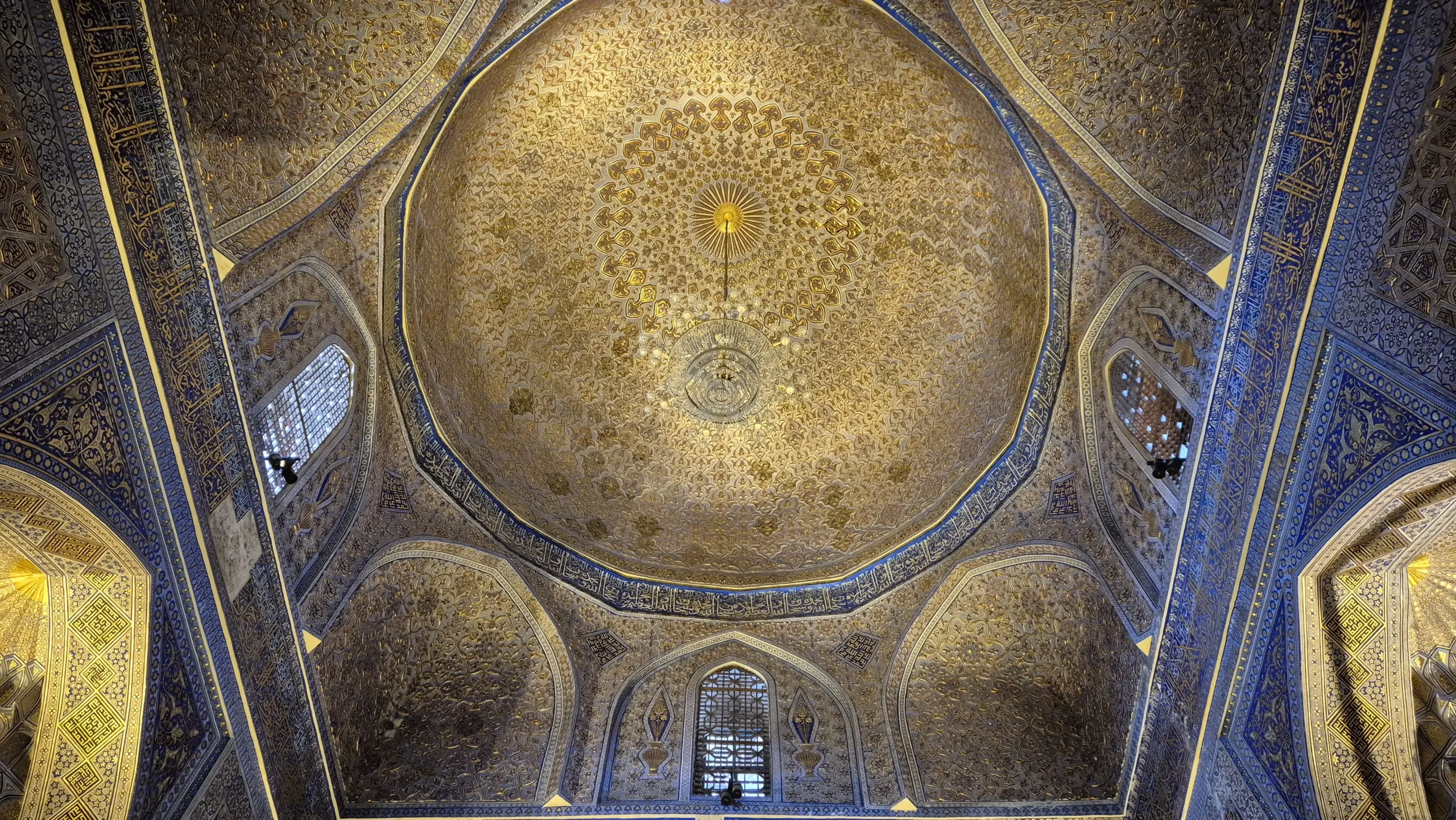 Inside Gur-e-Amir, Samarkand a photo of the ceiling of the mausoleum that houses Amir Temur's remains is entirely tiled. There is a central dome with tiles in gold leaf in a circle. There is a band all the way round of deep blue with a script on it. Gur-e-Amir, Samarkand, Uzbekistan