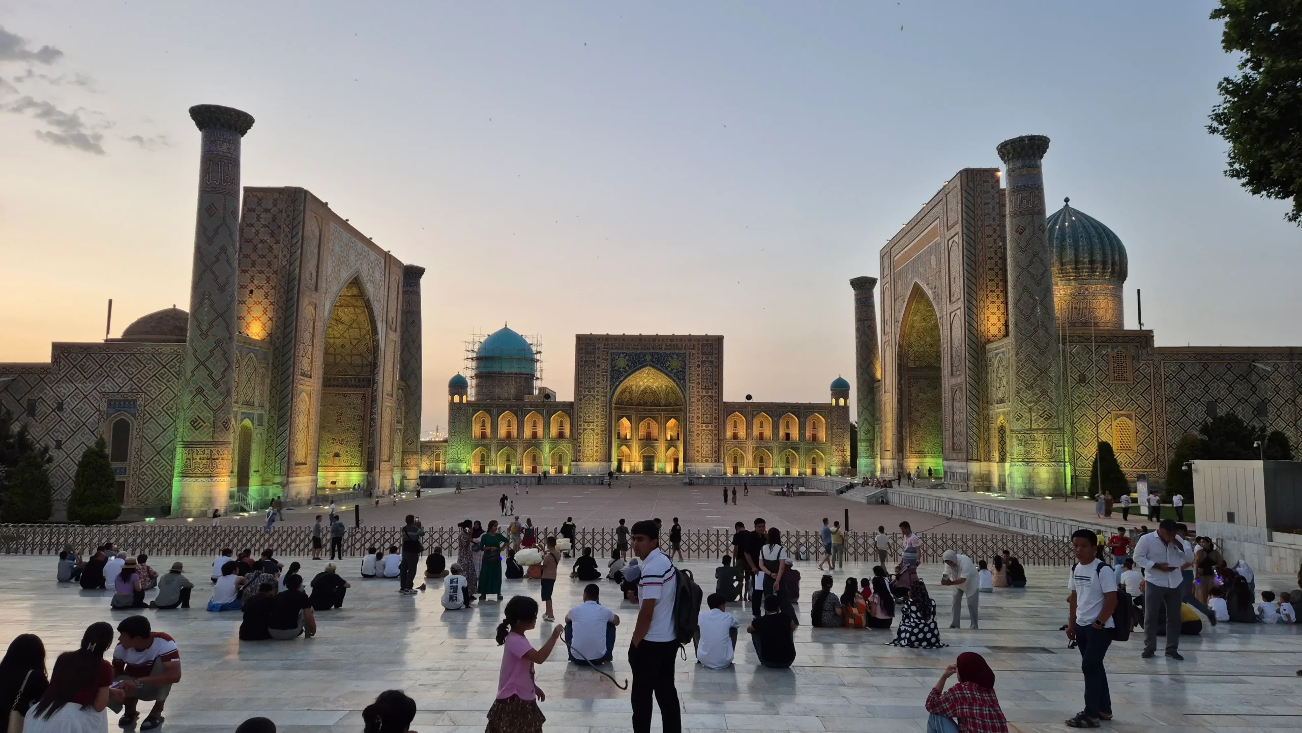 Registan Square, Samarkand Registan Square at sunset has three ancient Silk Road madrasahs facing each other with tall minarets, blue domes and facades with intricate tiling. There is a yellow green lighting on the buildings in Registan, Samarkand, Uzbekistan