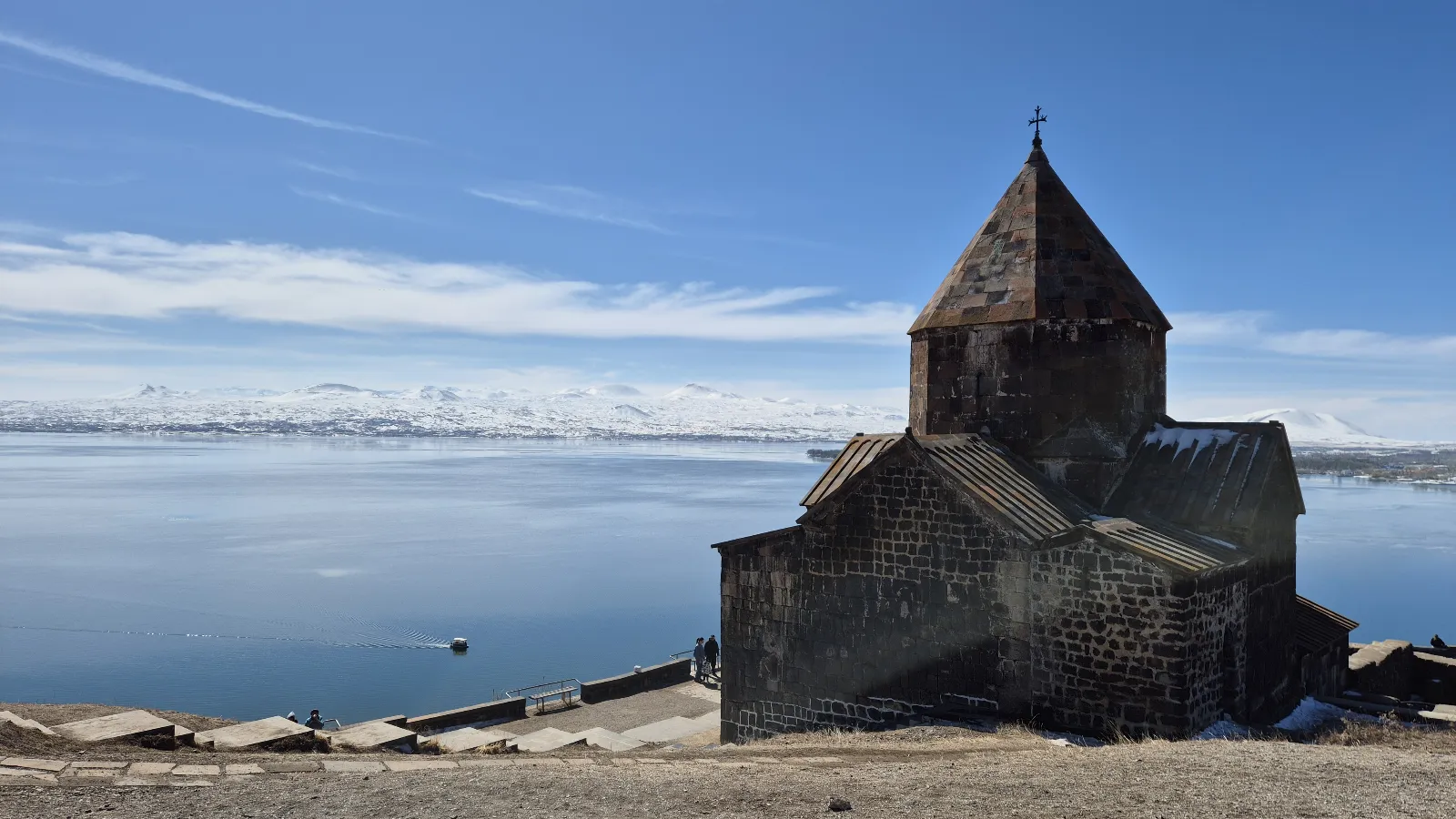 a dark brick monastery (Sevanavank) sits on a hill overlooking Lake Sevan and the surrounding snow-capped mountains, Armenia