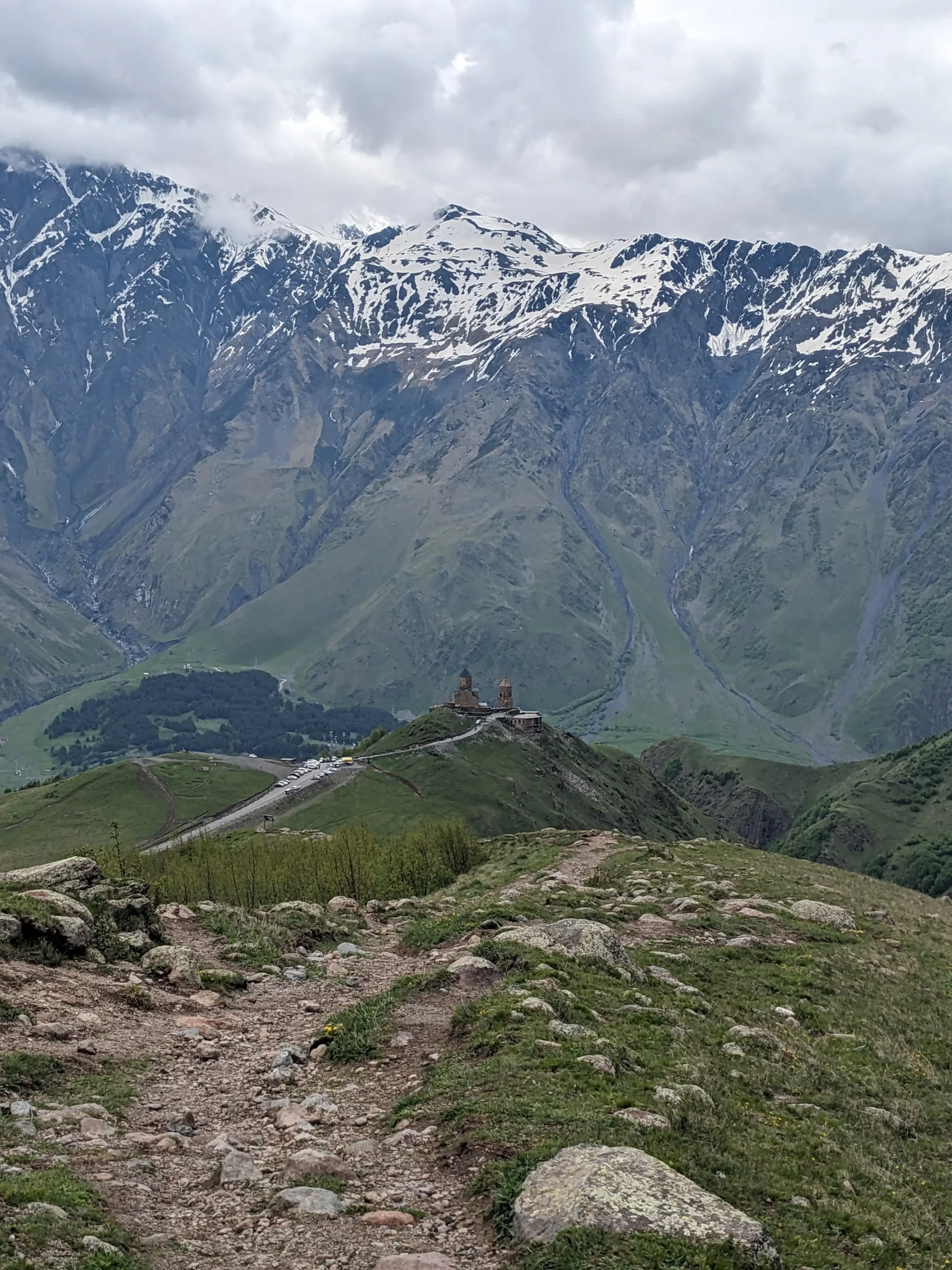 Gergeti Trinity Church stands on a green hill with snow-capped mountains in the background in Kazbegi (Stepantsminda), Georgia