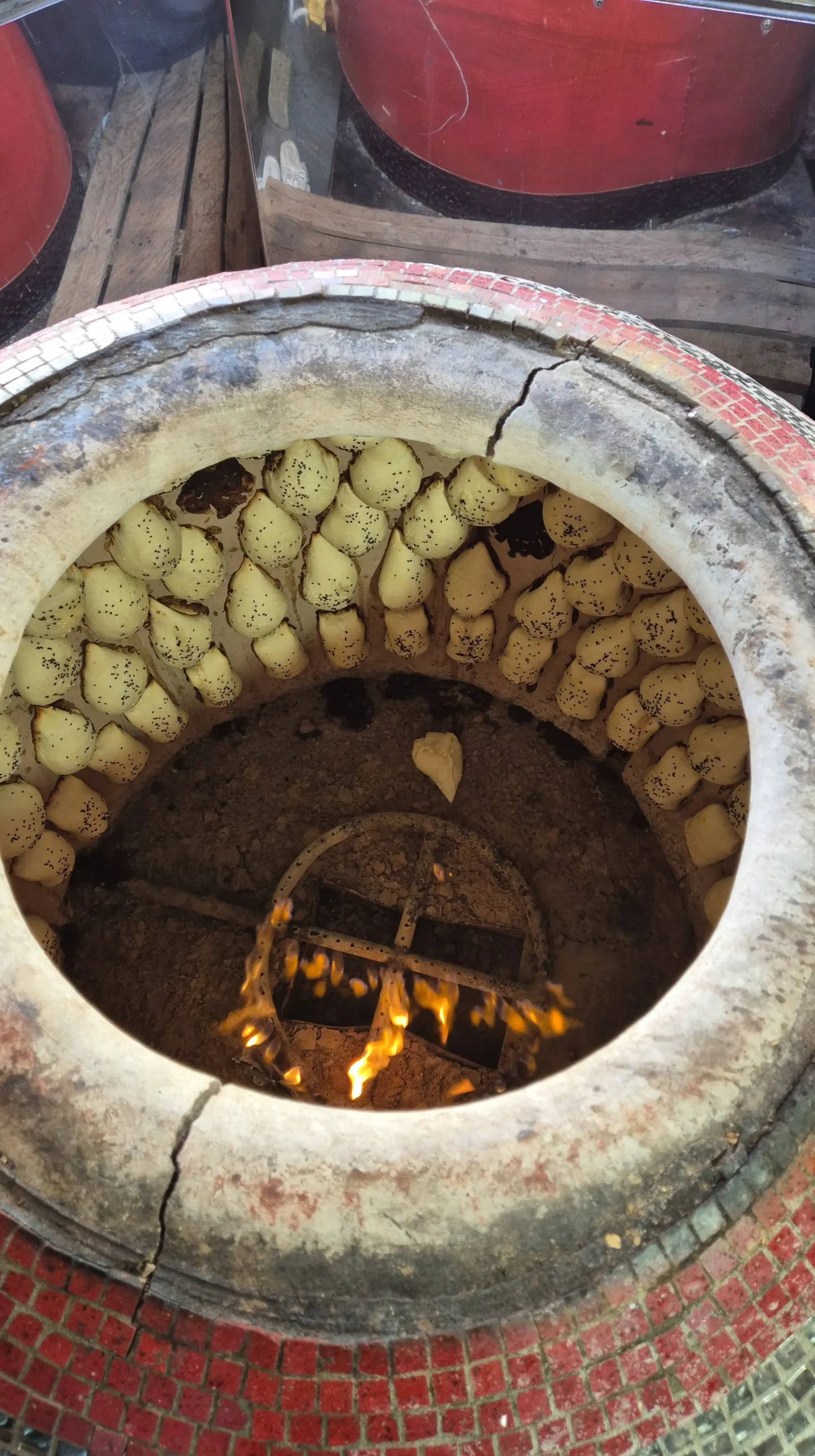 Uzbek samsa a close up shot of the inside of a working Uzbek tandoor shows flames at the bottom and uncooked dough parcels stuck to the inside walls while they cook