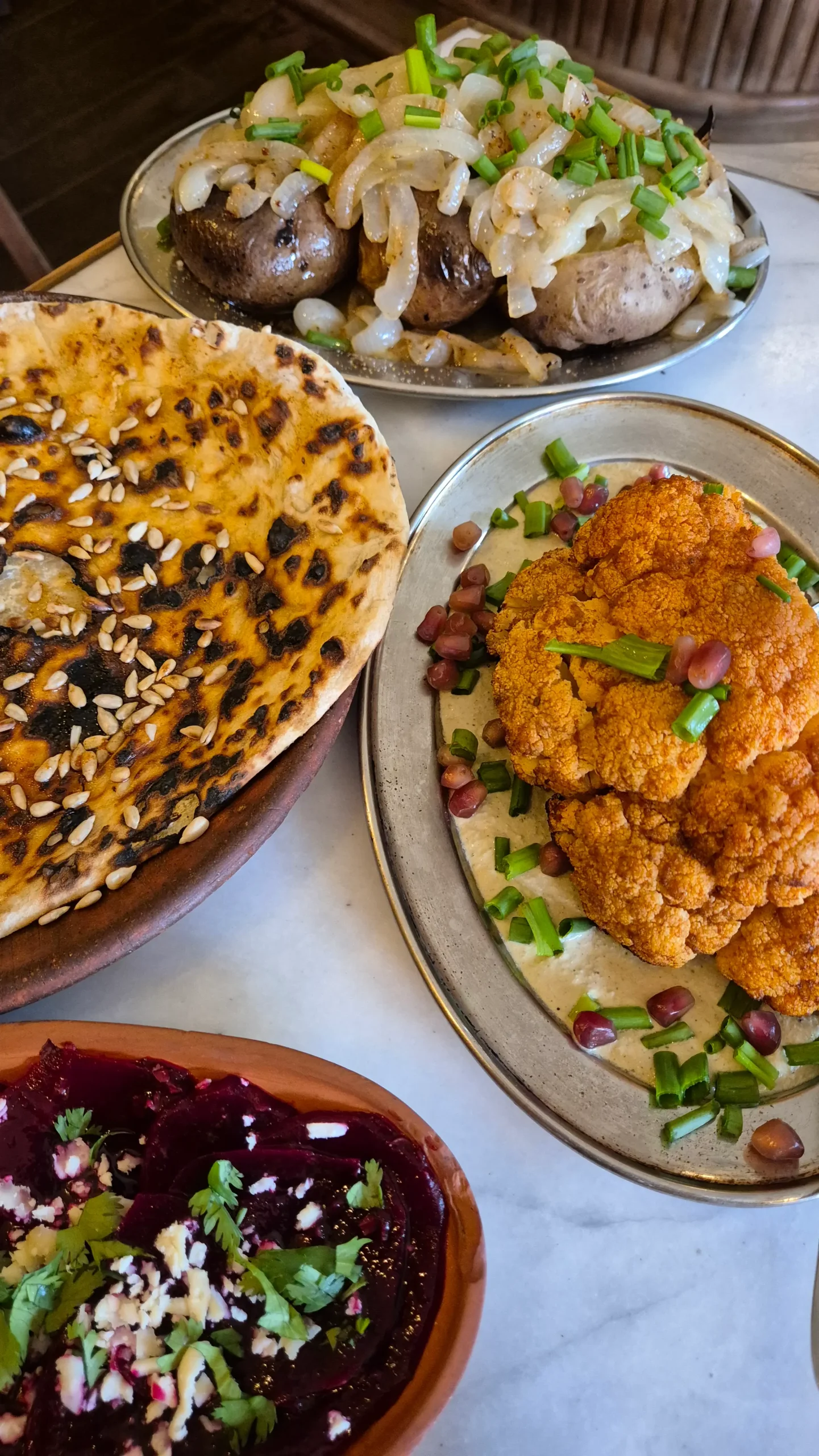 Delicious dinner at Doli a table of food - potatoes with garlic and onion, roasted cauliflower with bazhe (walnutty) sauce and pomegranate, a flatbread covered in Kakhetian sunflower oil and sunflower seeds
