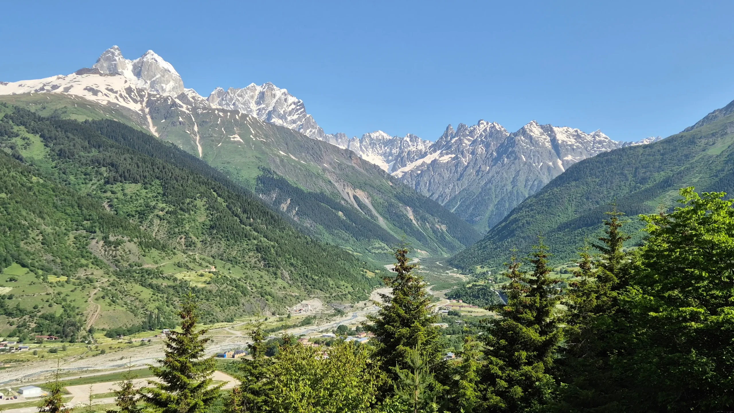 a view over the Svaneti mountains of north west Georgia shows snow-capped mountains, a valley and green rolling hills along the hike from Mestia to Ushguli