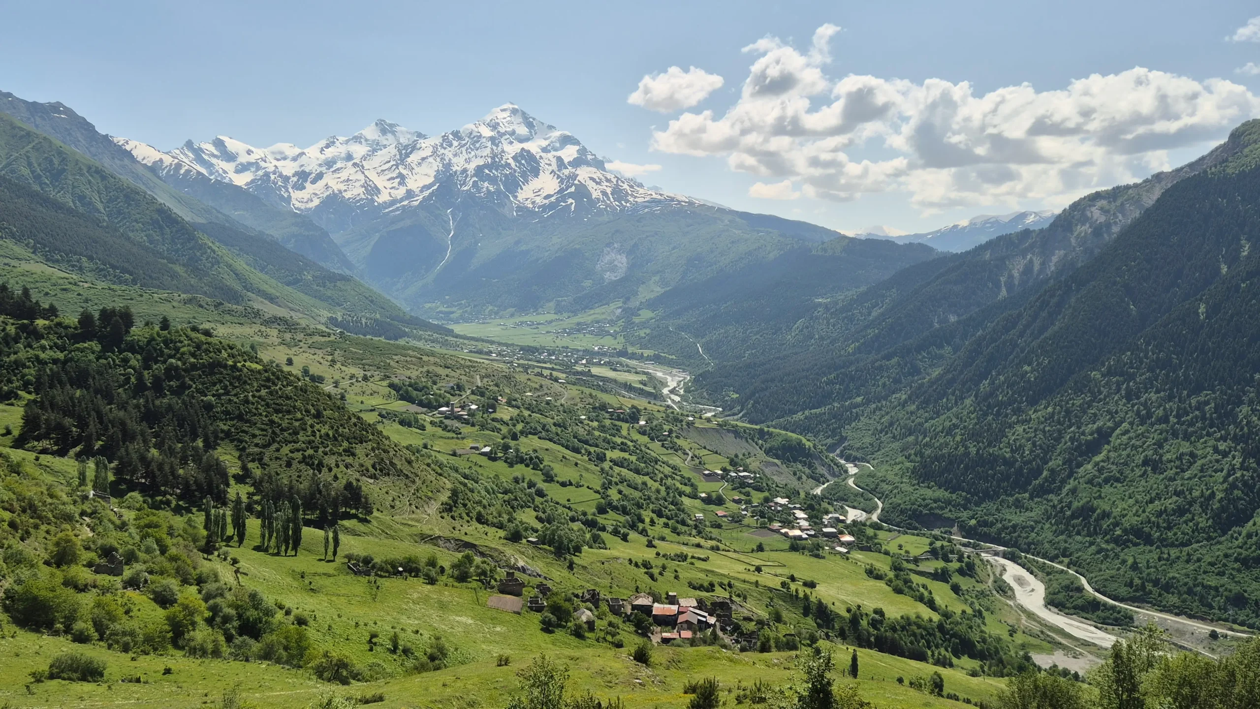 View over the valley: Mestia to Zhabeshi a view in to a green valley with a meandering river and snow-capped mountains on a hike from Mestia to Zhabeshi