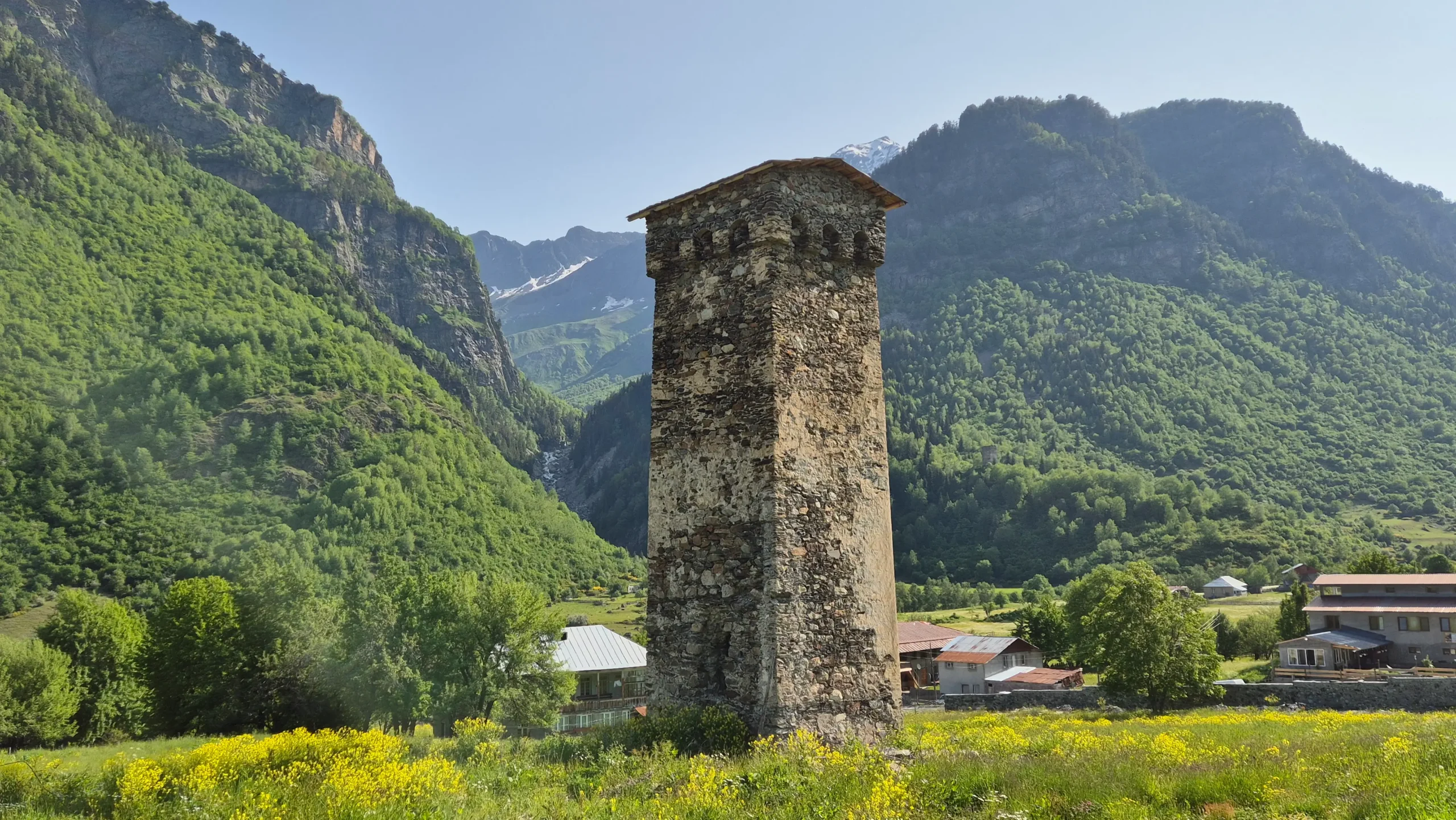 Svan tower in Zhabeshi a historic Svan watchtower stands in the centre of a valley with green trees either side on the Mestia to Ushguli trek