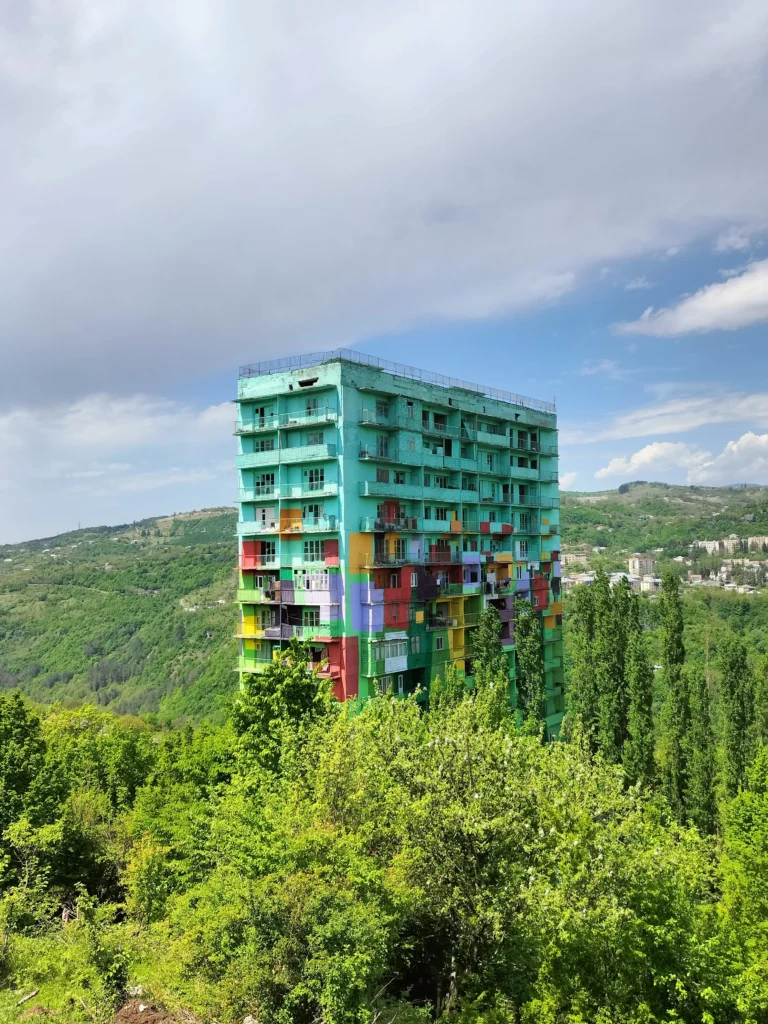 a lone apartment block painted in lots of different bright colours stands in a valley surrounded by green trees in Chiatura, Georgia