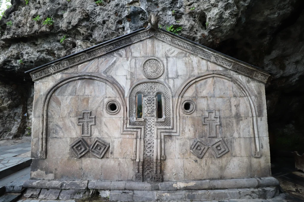 a historic church built in to a cliff face in Chiatura has two slot windows, two crosses, and two squares at jaunty angles as decoration - Mgvimevi Convent, Georgia