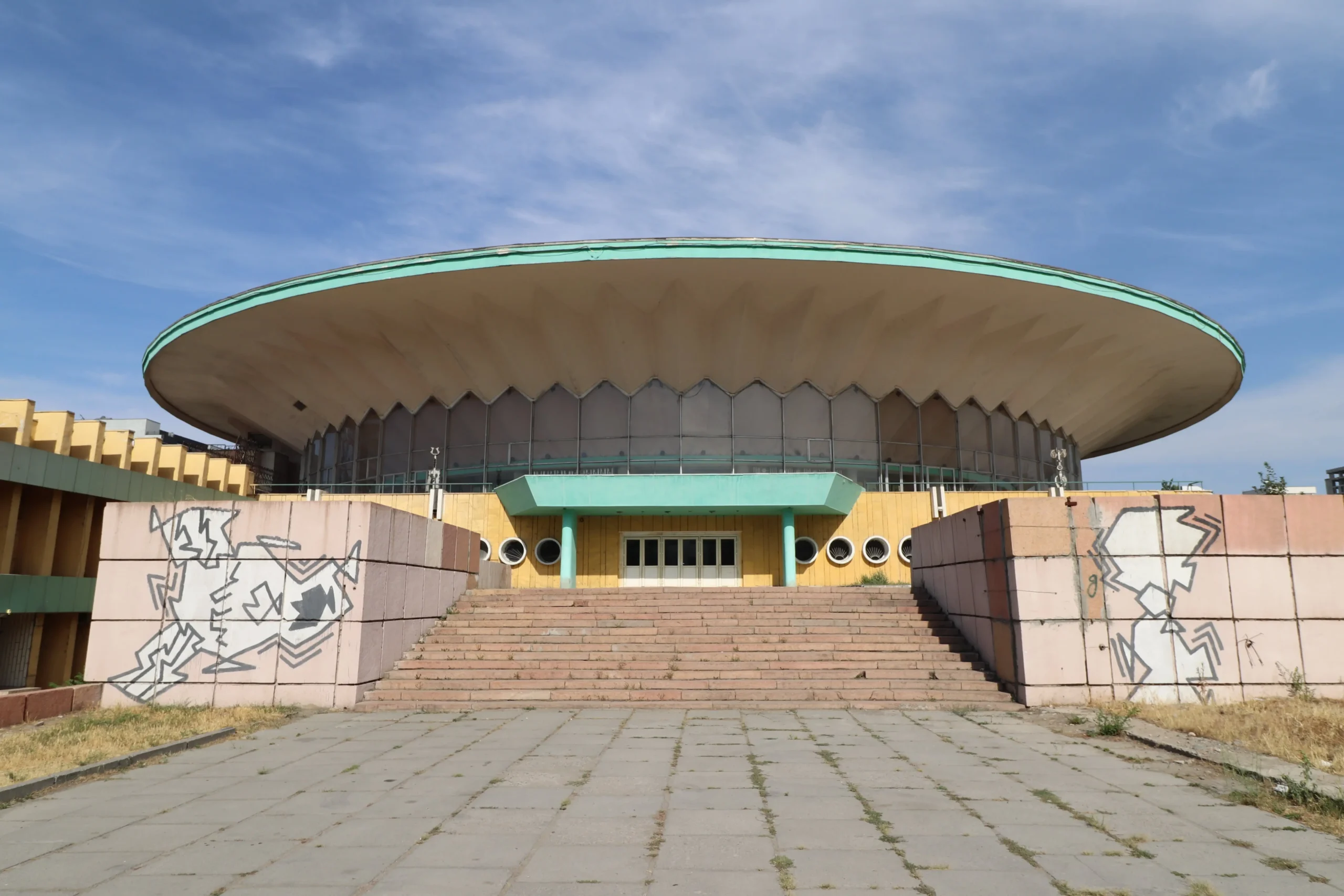 Bishkek Circus stairs lead up to a yellow and green building that has a UFO Soviet style to it - State Circus, Bishkek, Kyrgyzstan