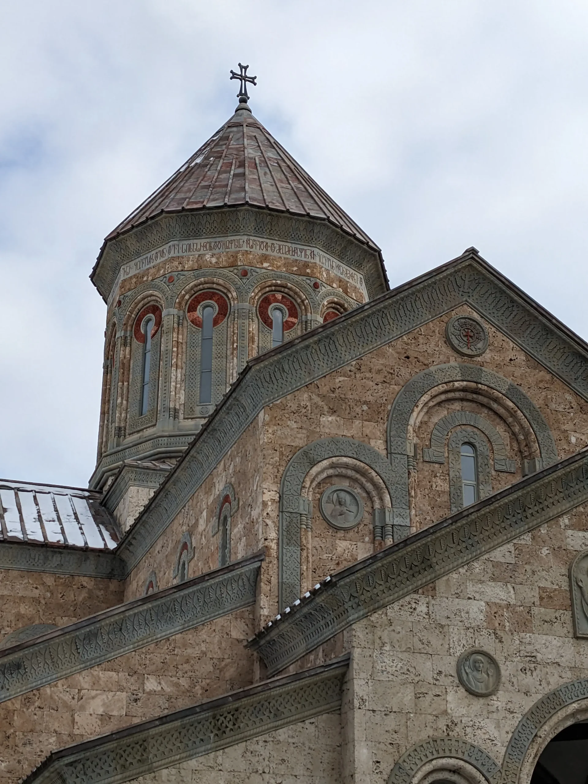 Bodbe Monastery a close up of Bodbe Monastery shows tall, thin windows surrounded by green and red stone, Georgian inscription and a cross on the top, Sighnaghi, Georgia