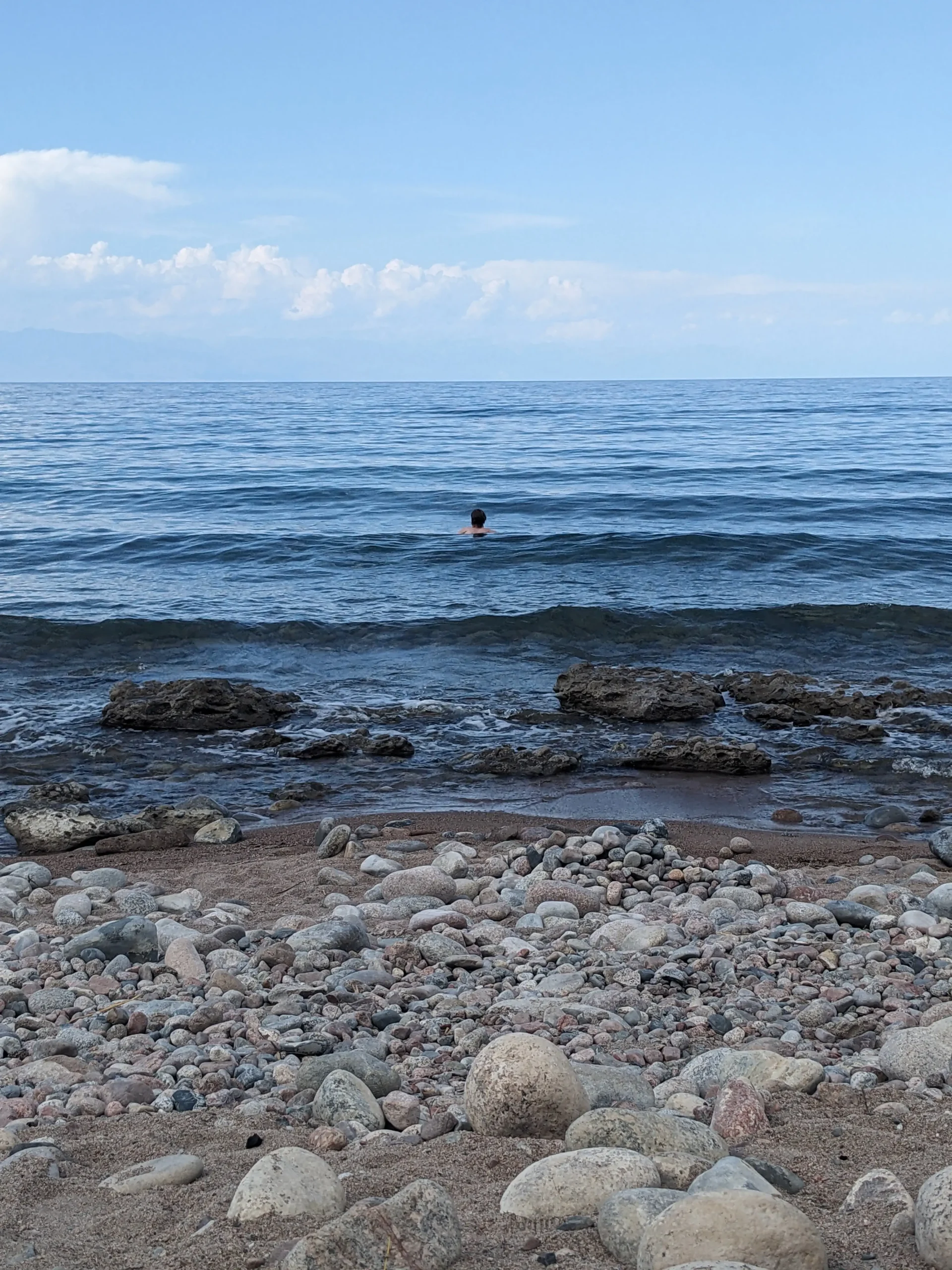 a man is swimming in Issy Kul lake in Kyrgyzstan. There are small waves and a pebbly shore