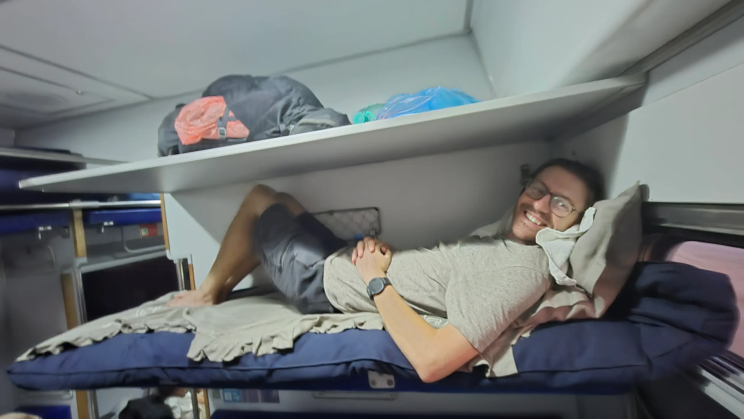 a man is laying down in a confined sleeper train bunk