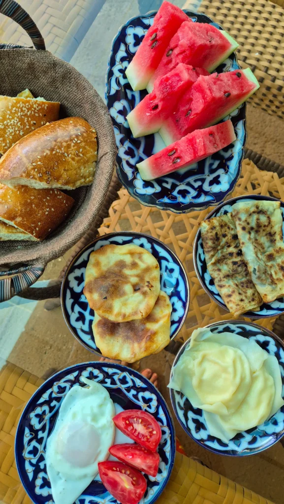 Bekhzod Breakfast a vegetarian Uzbek breakfast spread of fried eggs, tuxum barak, somsa, bread, watermelon and flatbreads stuffed with greens
