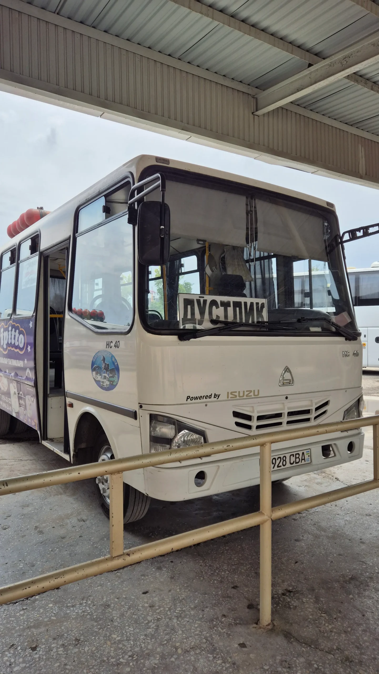 a white bus has 'Dostyk' in Russian written on a sign in the window in Andijan, Uzbekistan