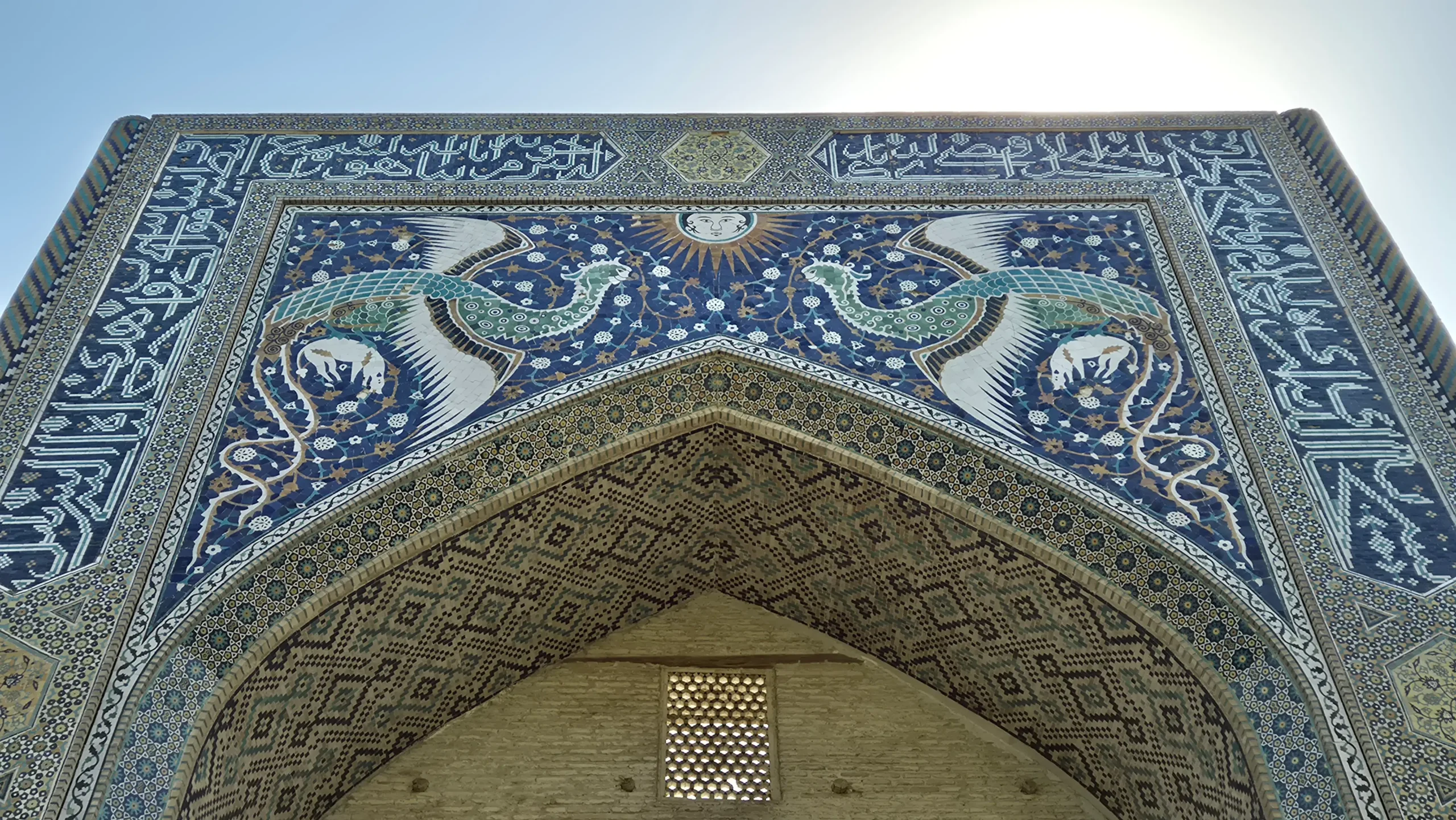Nadir Divan Begi Madrasah a close up of tiling on the front of a historic madrasah shows two birds and a sun with a face - Nadir Divan Begi Madrasah, Bukhara, Uzbekistan