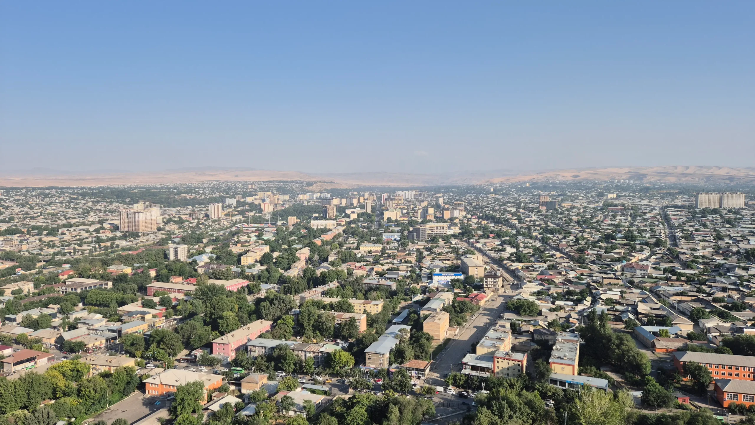 view over Osh in Kyrgyzstan of apartments, trees, and seemingly desert in the background.