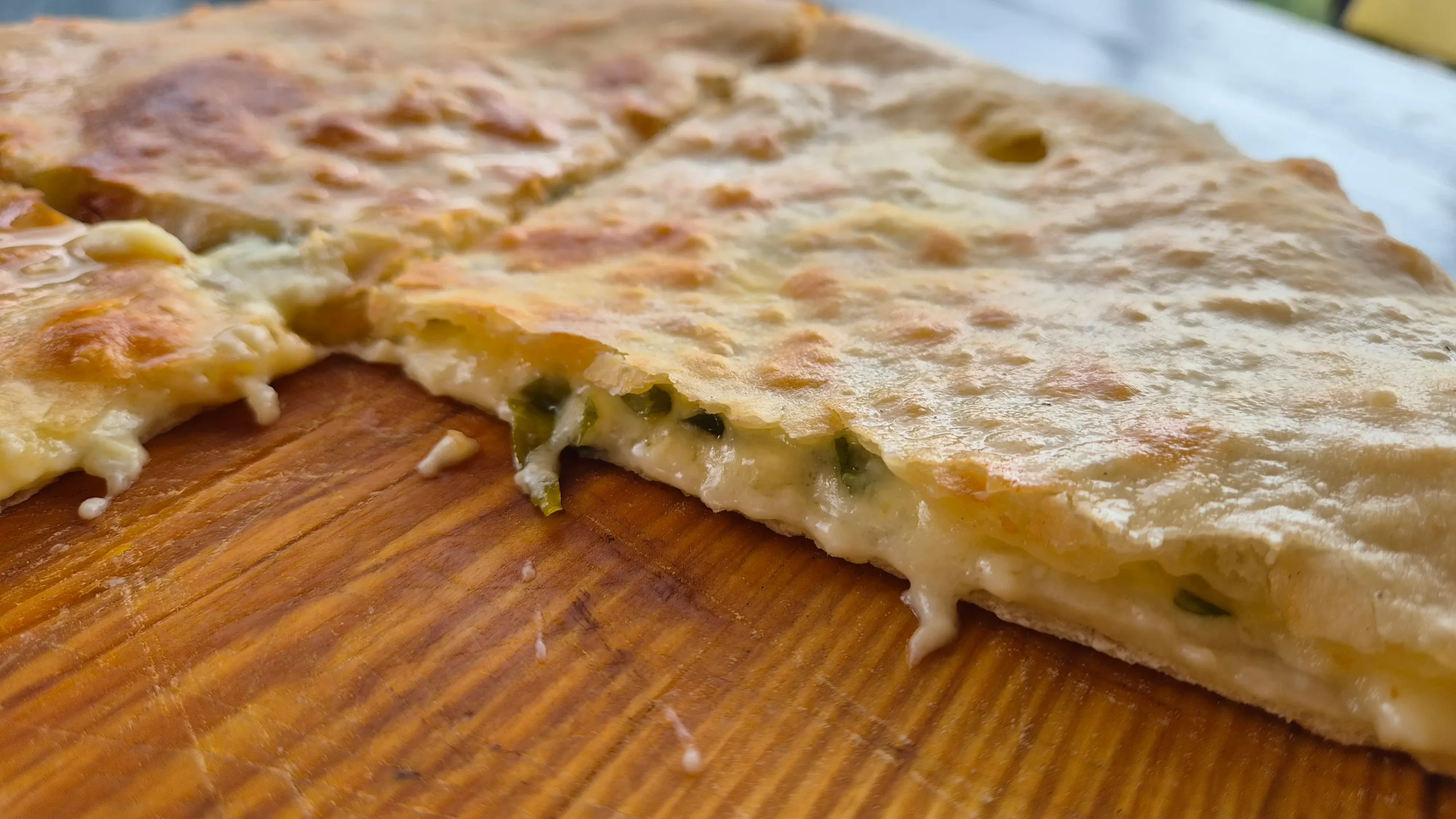 Svanetian Khachapuri a close-up of a khachapuri (cheese-stuffed bread) that shows the melted cheese and spring onion mixture oozing out the side