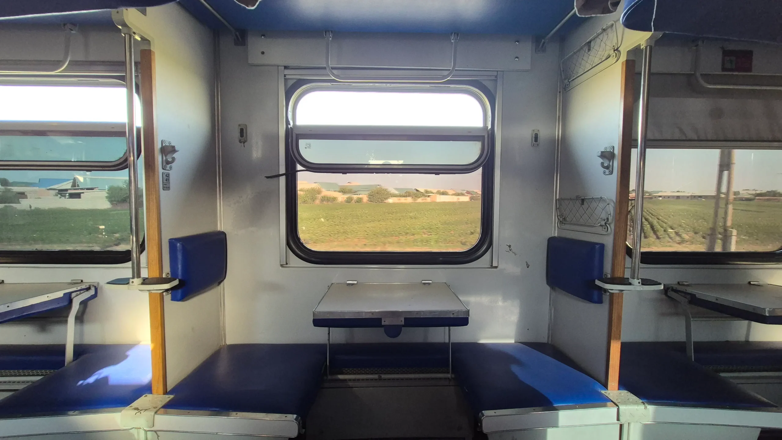 Classic setup of an Uzbek sleeper train an open train carriage of Uzbek Railways third class cabin has two seats with blue cushions separated by a fold away table and a large open window