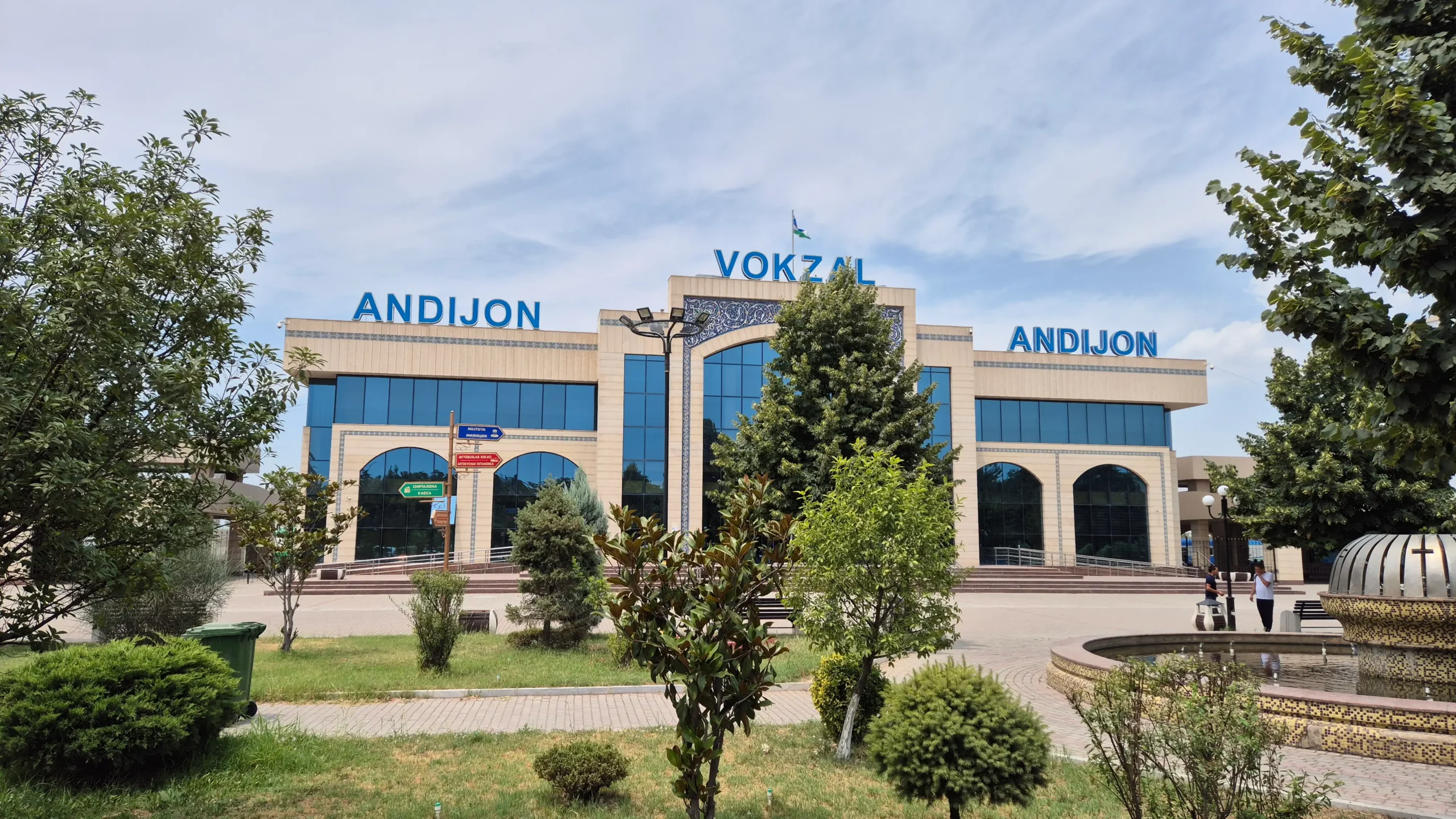 Andijan Train Station is a large brick and glass structure with a green park in the front