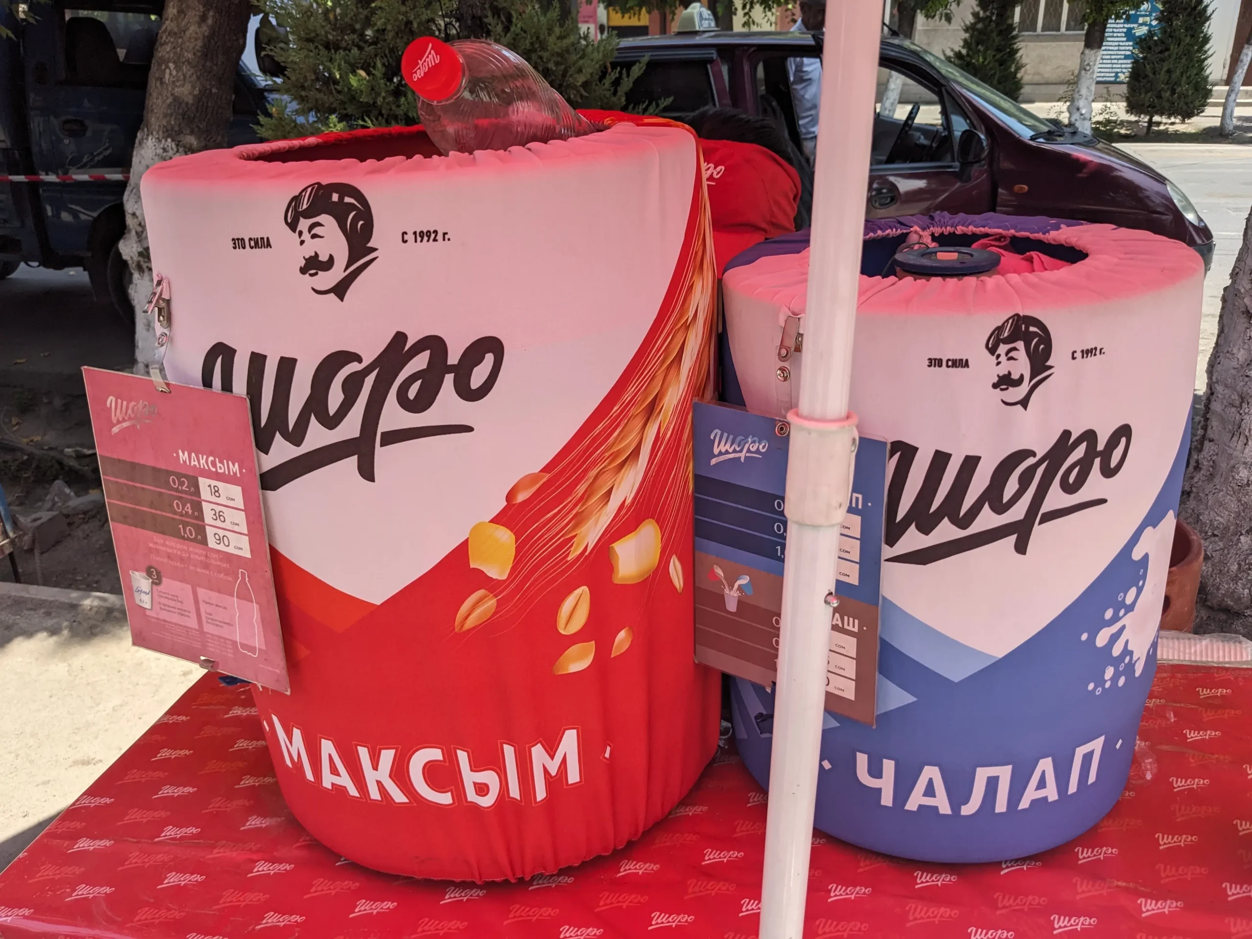two large containers on a stand at the side of the street in Osh, Kyrgyzstan, are filled with two local Kyrgyz drinks - chalap and maksym