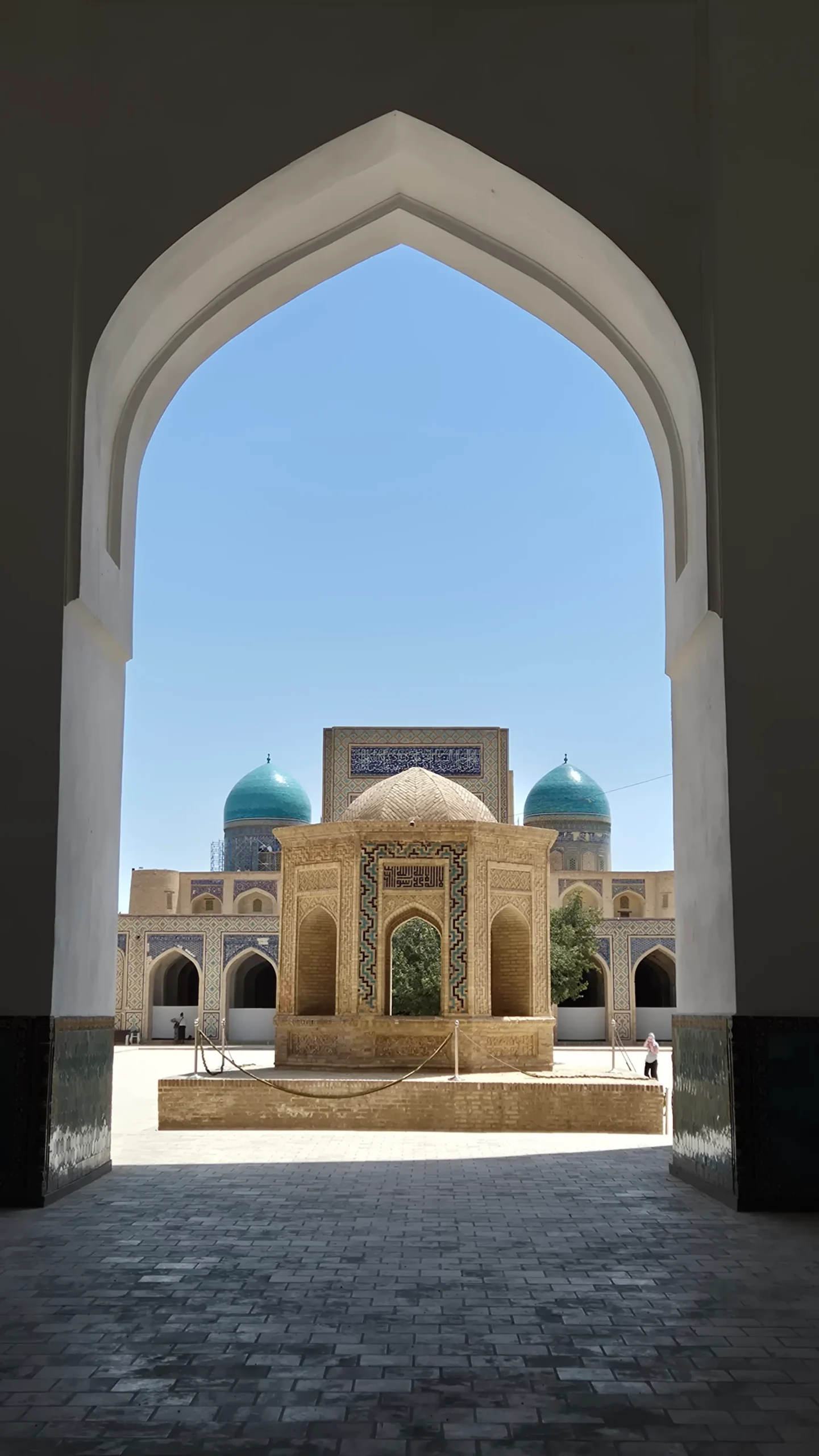Kalon Mosque an archway leads to a mosque courtyard with smaller brick structure and two light blue tiled domes in Bukhara, Uzbekistan