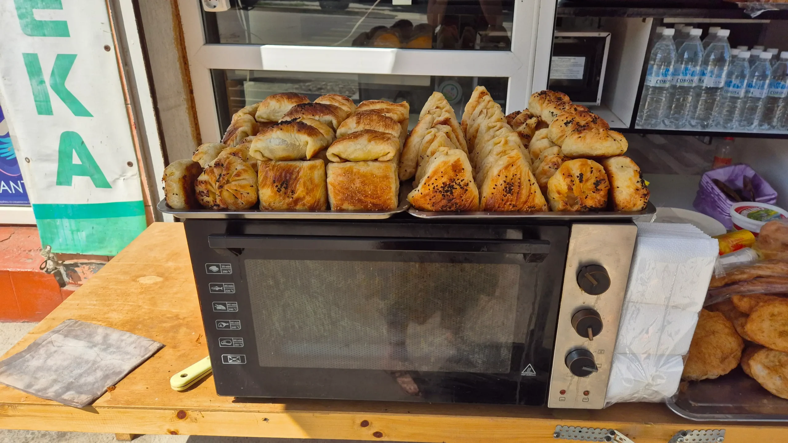 a microwave on the side of the street has two baking trays of different types of somsa in Osh, Kyrgyzstan