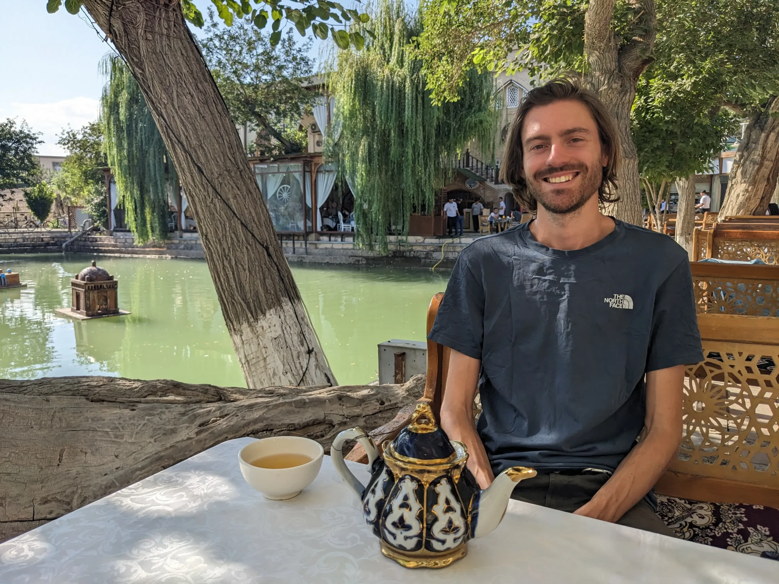Lyabi Hauz Ensemble a man sits at a table beside a pond with a pot of tea
