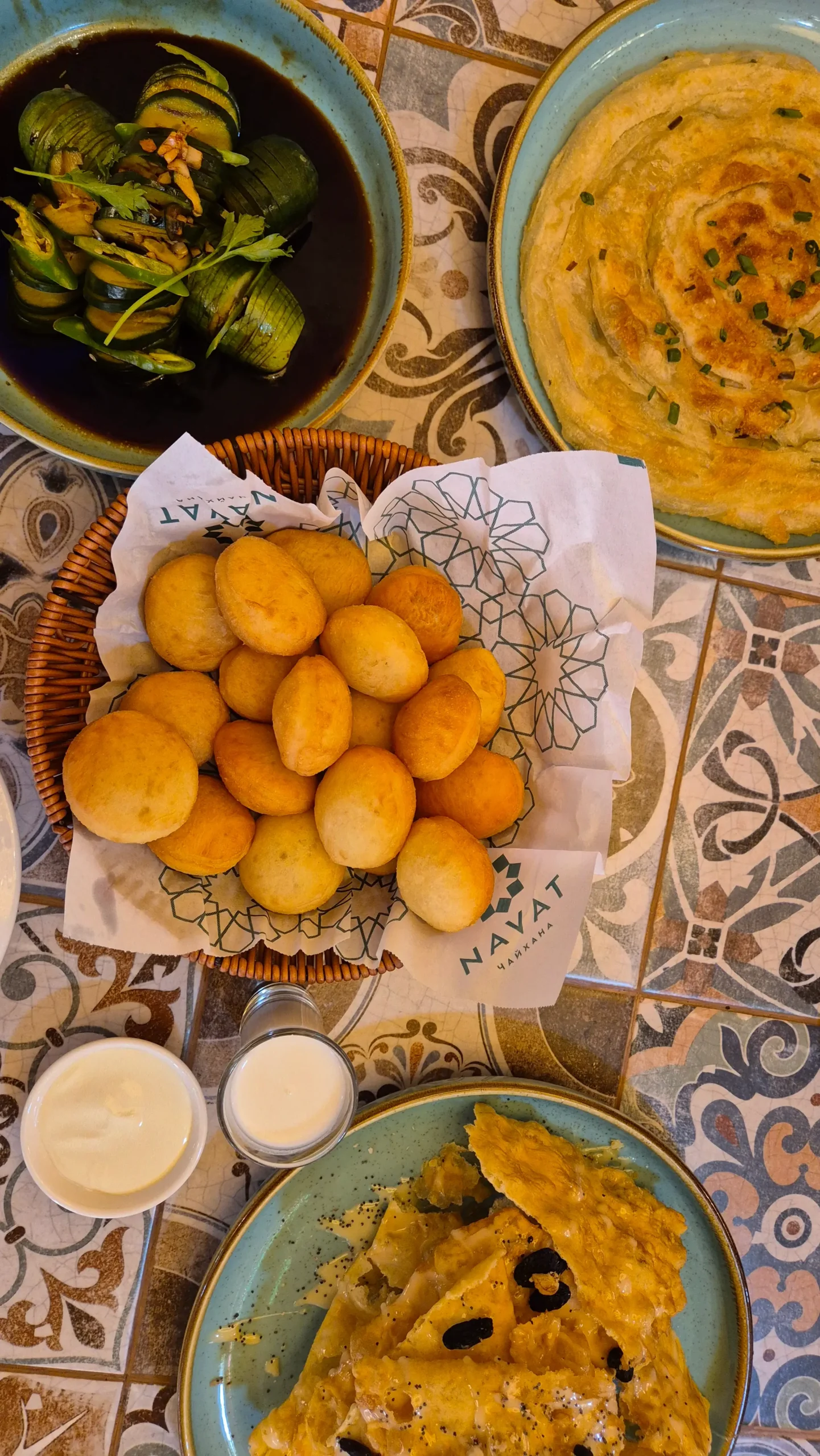 a spread of Kyrgyz vegetarian food consists of boorsok (fried dough) and kaymak (sour cream), a cucumber salad with soy and garlic dressing, and kattama (a chewy, layered flatbread) at Navat, Osh, Kyrgyzstan