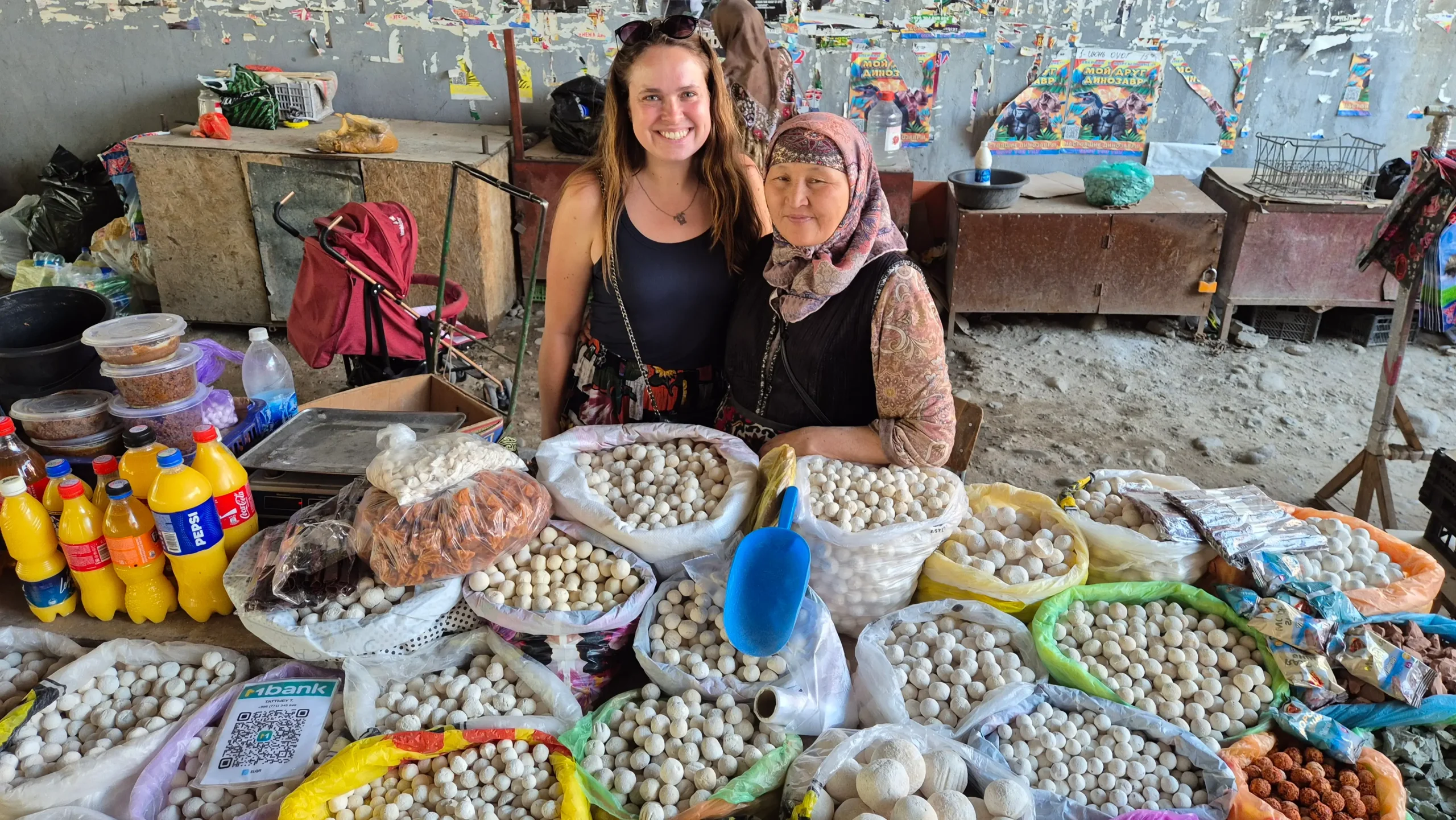 a woman has a picture with a woman who owns a stand selling qurut at Osh market. The stand is full of different types of qurut.