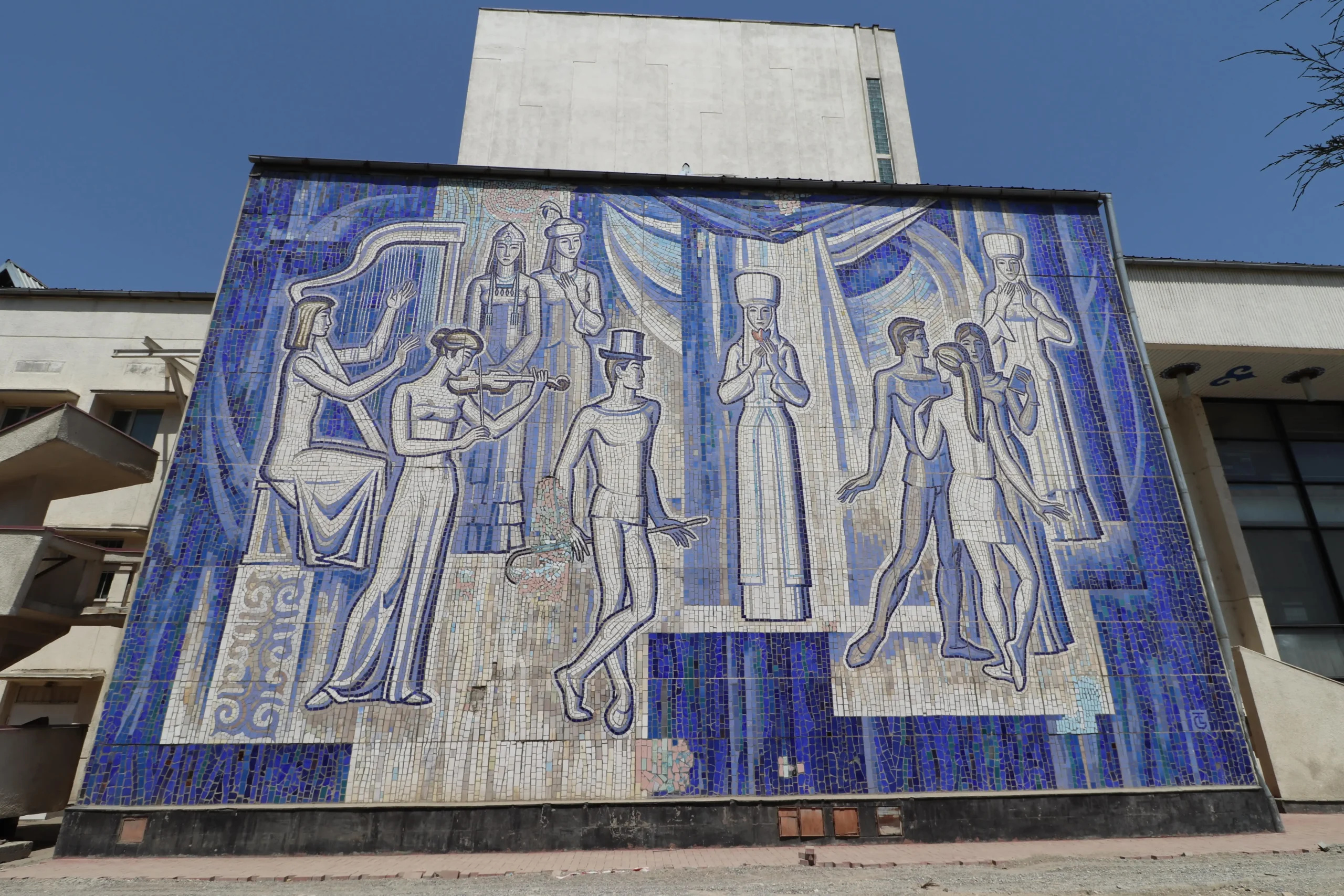 a Soviet mosaic mural made from blue and white tiles shows musicians, dancers, and performers in Osh