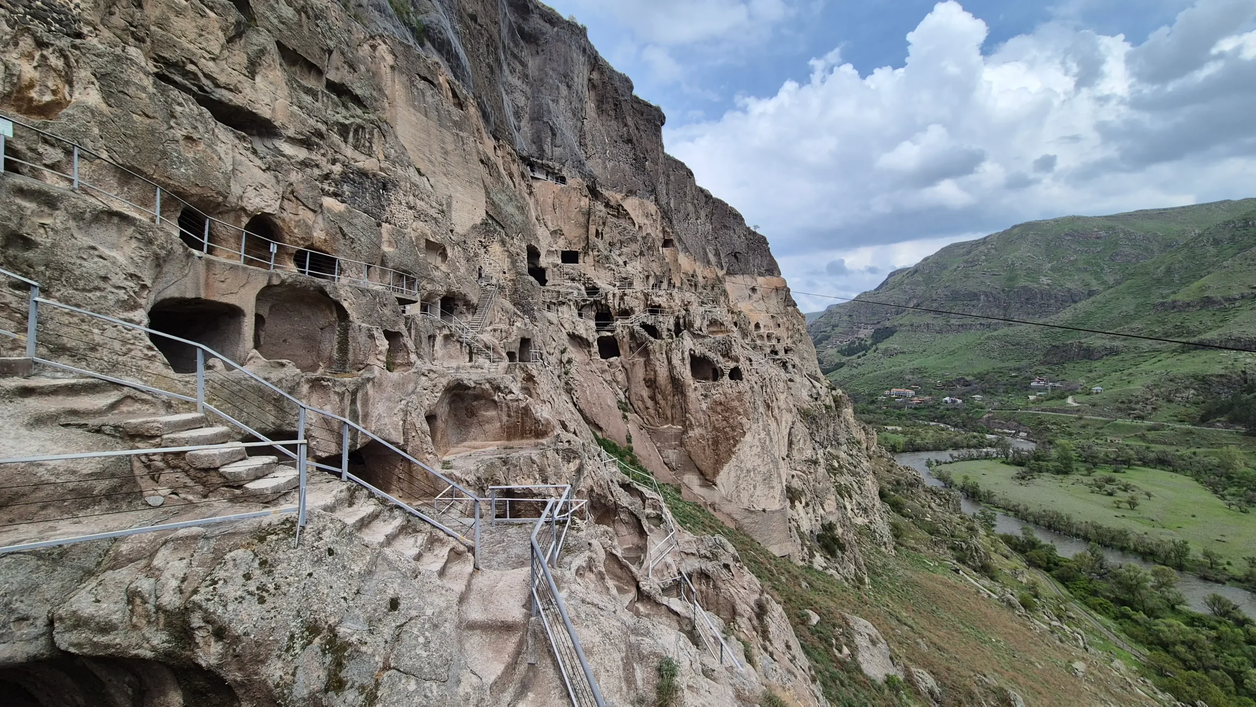 Vardzia Vardzi cave city built into a cliff face with original steps, openings, and tunnels. It overlooks a green valley with a river running through in Georgia