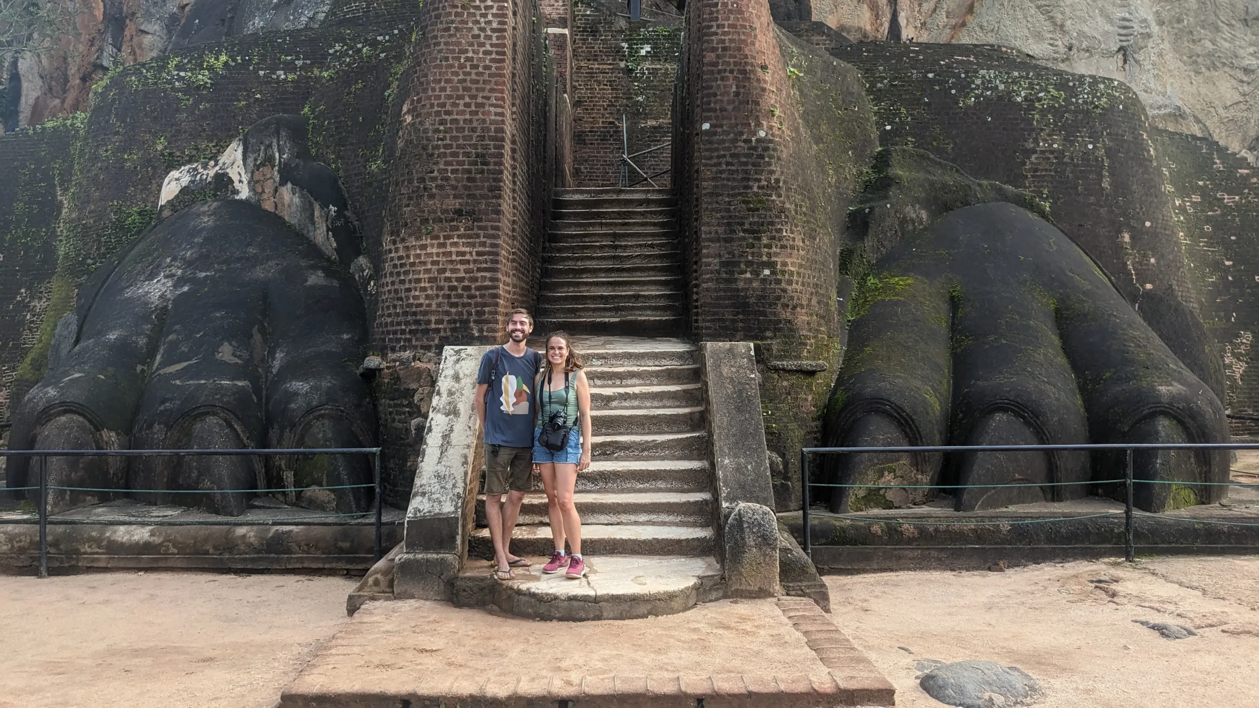 two people are standing at the bottom of a stone staircase in between two huge stone lion paws at Sigiriya Rock, Sri Lanka
