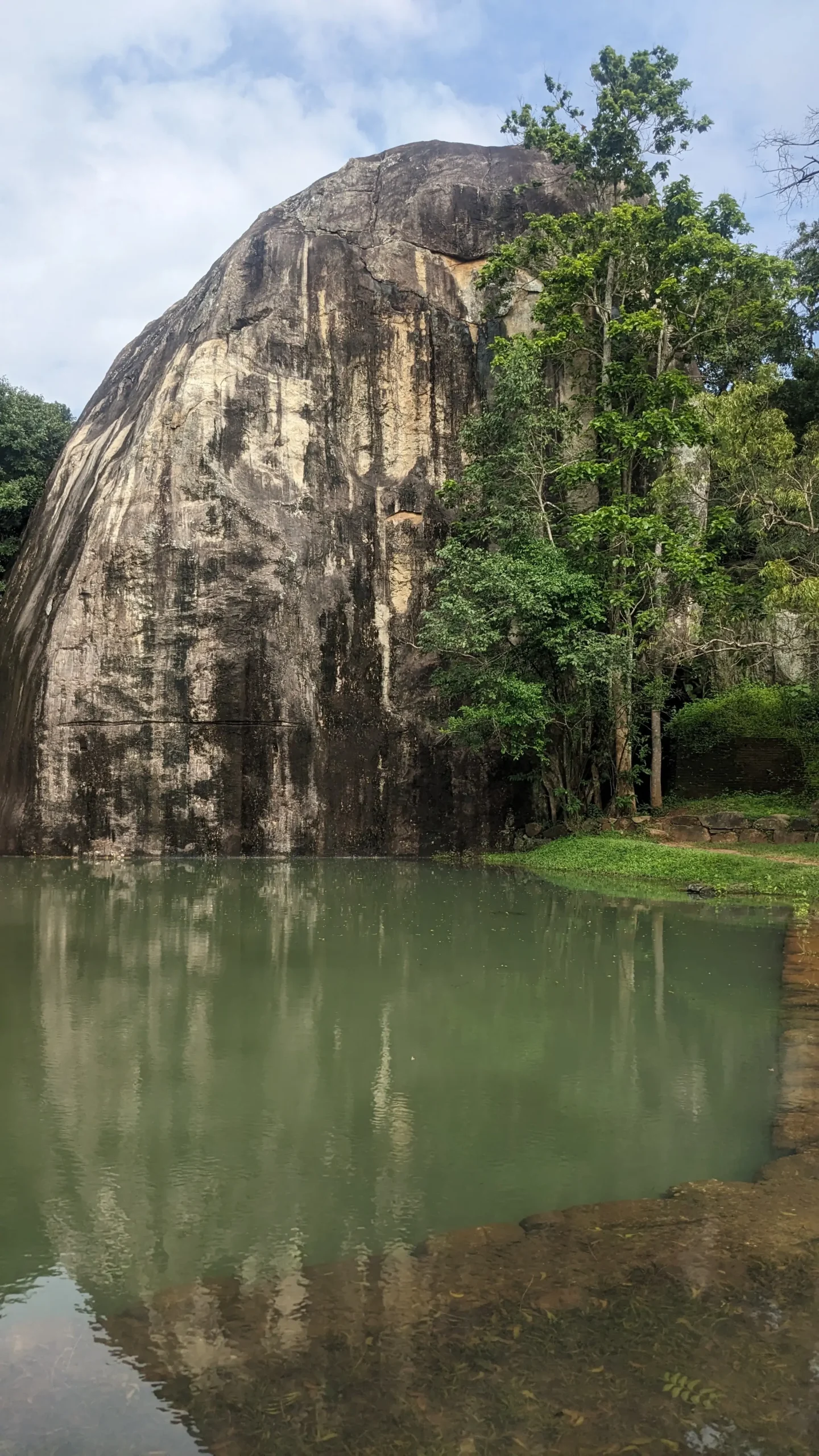 an octagonal shaped pond is filled with green water and backs onto a tall grey rock in Sigiriya
