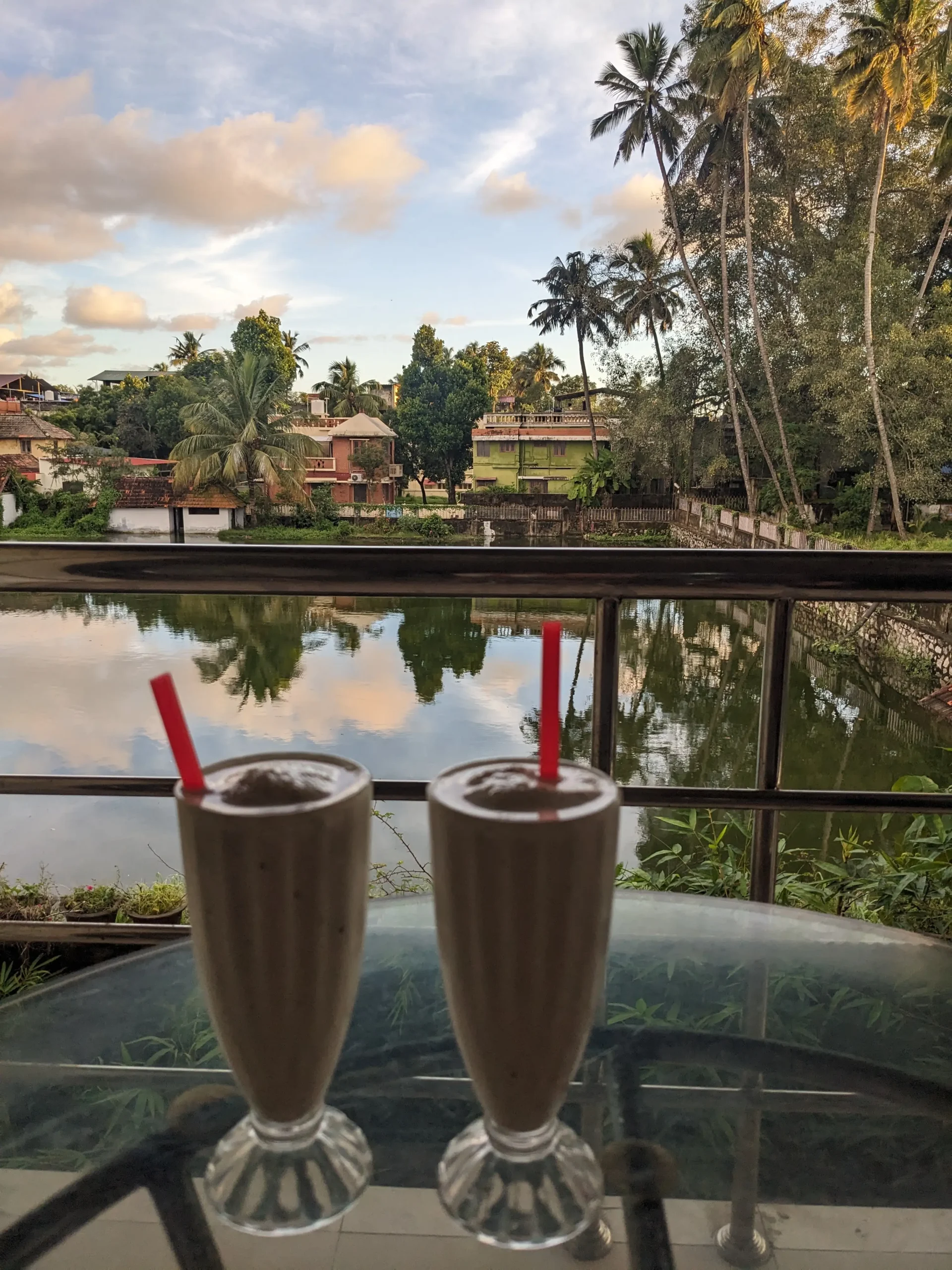 Two glasses of a creamy coconut shake sit on a table in front of a lake surrounded with palm trees in Trivandrum, Kerala, India
