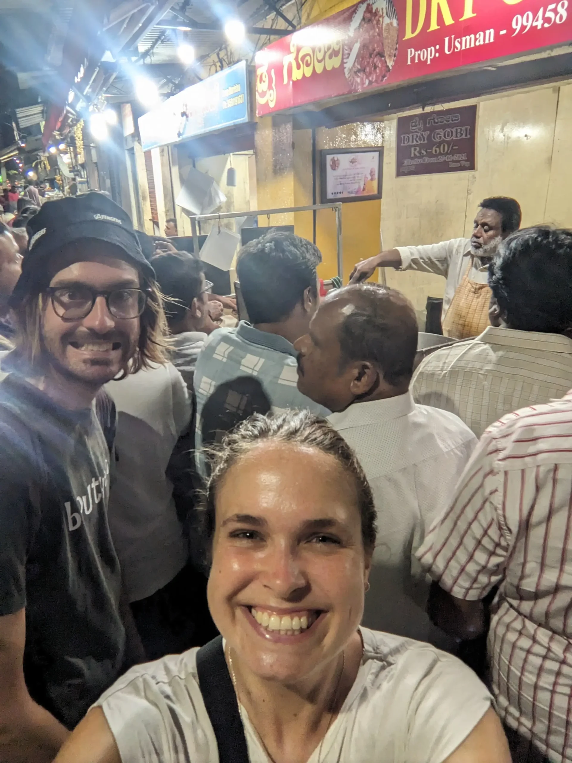 a crowd of people are shoulder to shoulder waiting for their portion of dry gobi to fried in Mysore, India