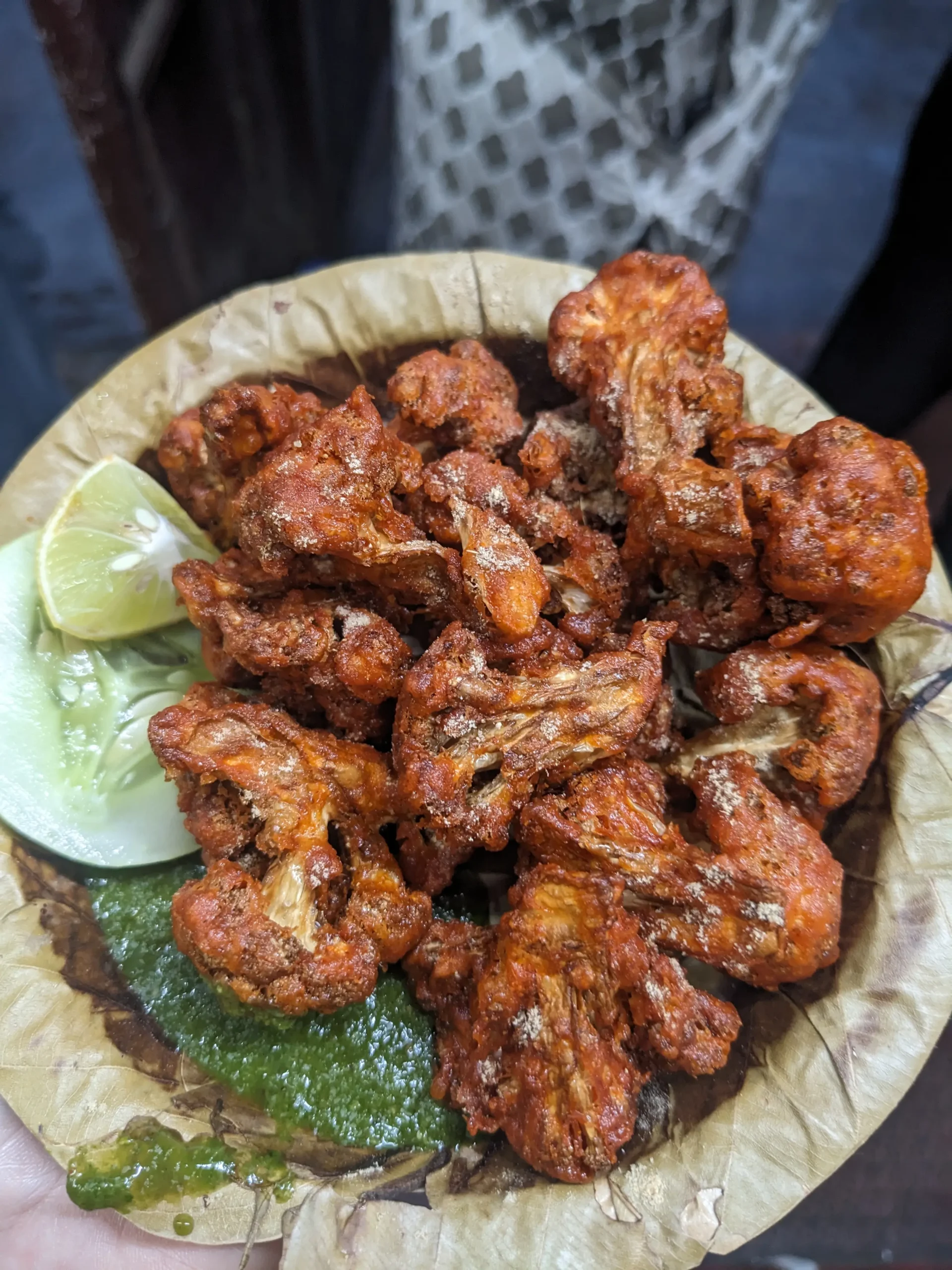 a plate made of dried leaves holds deep-fried cauliflower (or dry gobi) with a mint chutney, a slice of cucumber and a wedge of lime. Usman Dry Gobi, Mysore, Karnataka, India