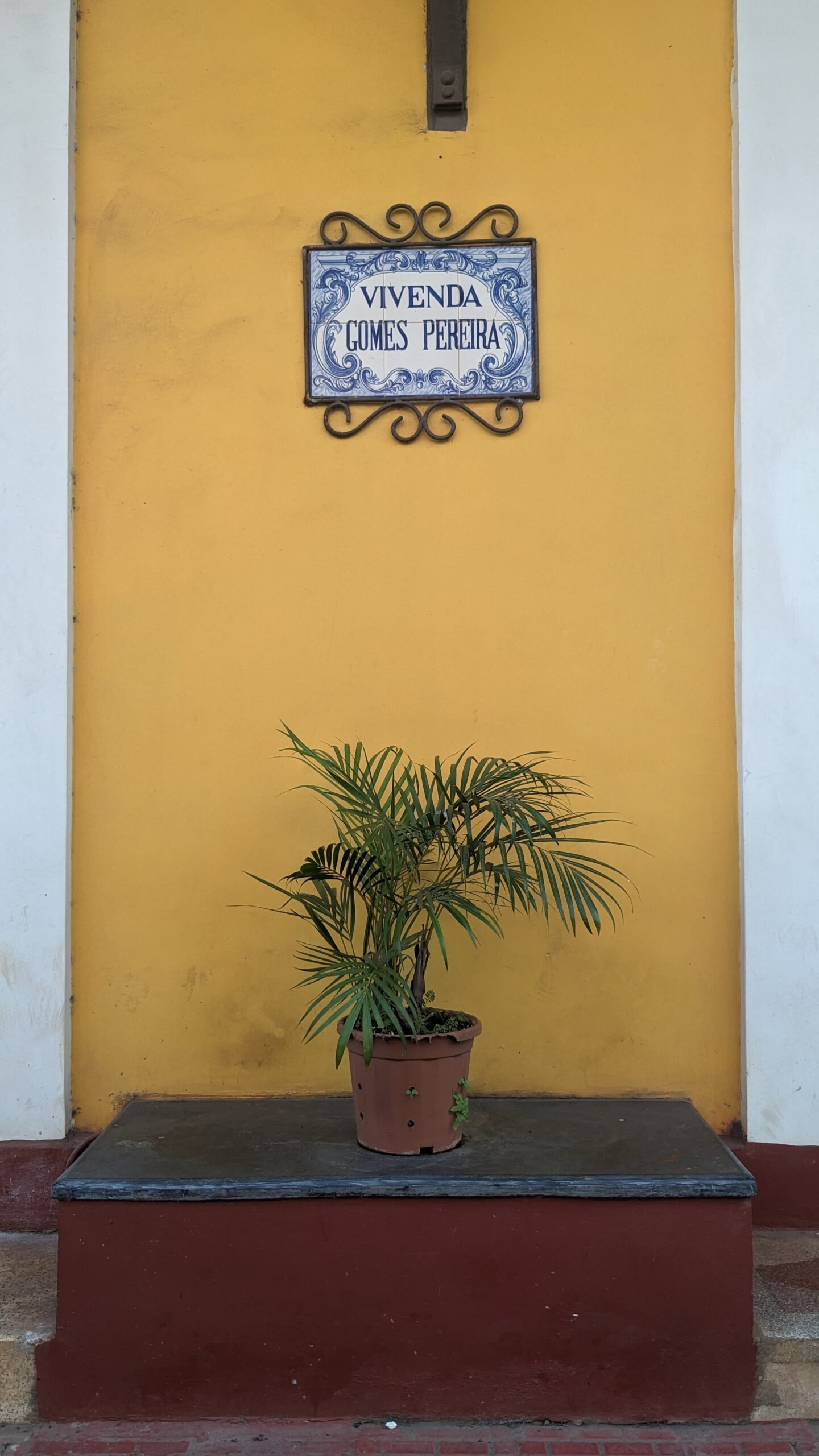 Panaji aesthetic a yellow wall with white edging has a small blue and white tile sign in the style of Portuguese azulejos and a potted plant in Panaji, Goa, India