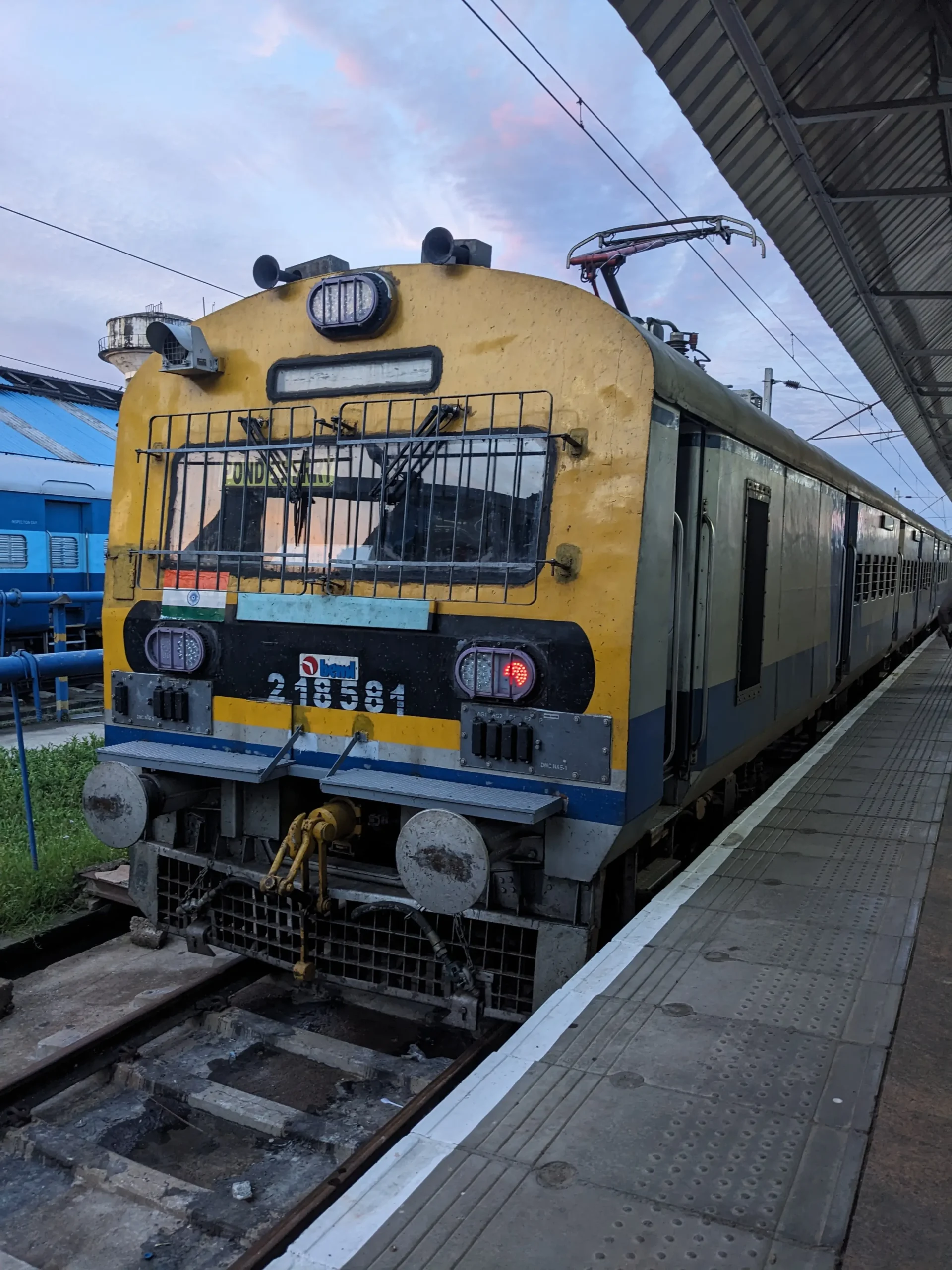 a yellow and blue Indian train is stopped at a station