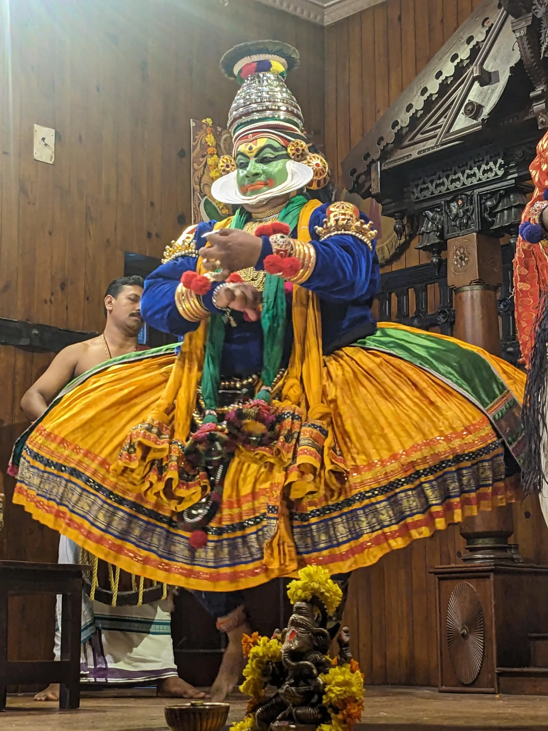 a Kathakali performer has a large yellow skirt and a green painted face in Kochi, Kerala, South India