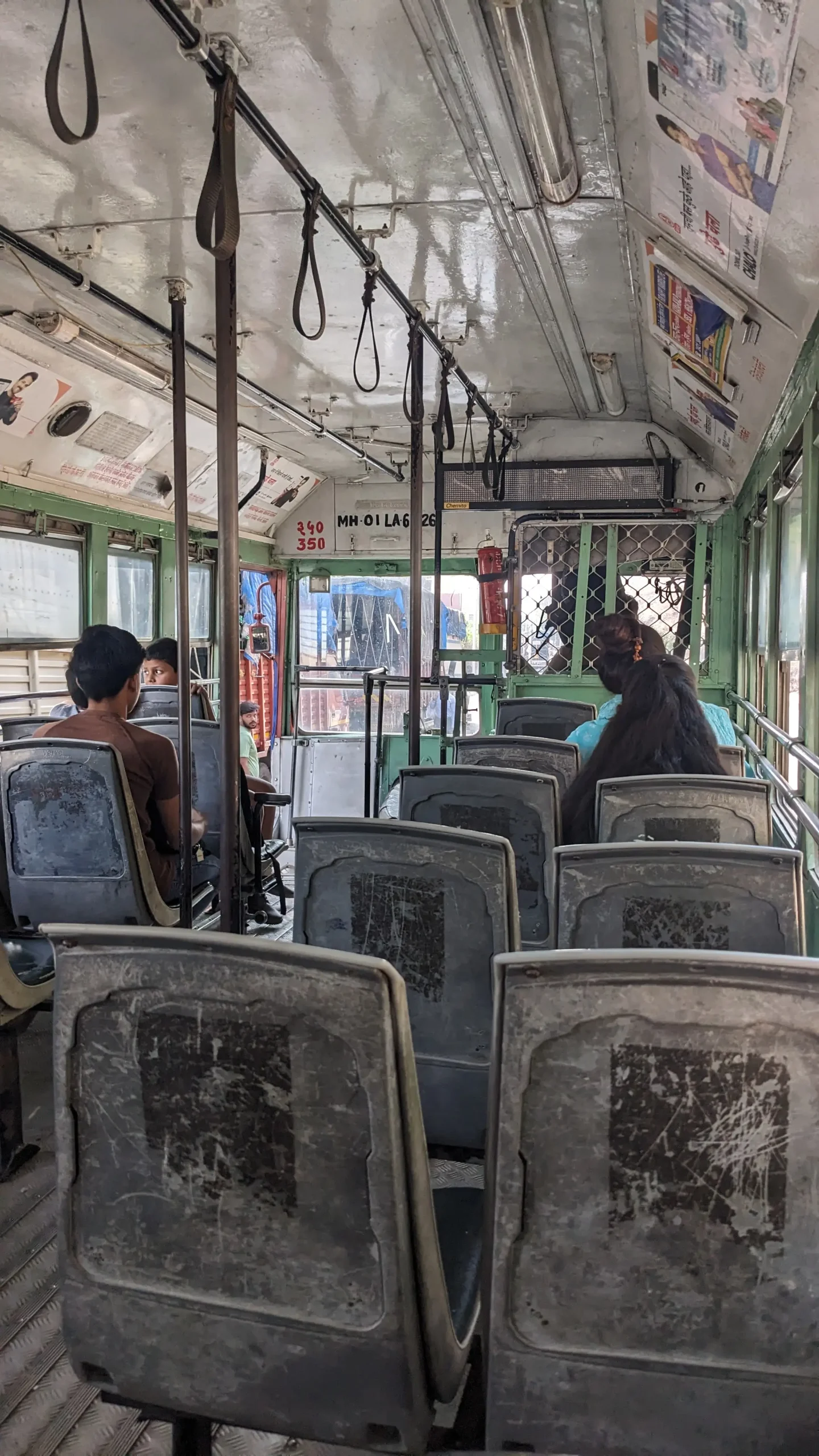 the inside of a local Mumbai bus has plastic grey seats and green walls