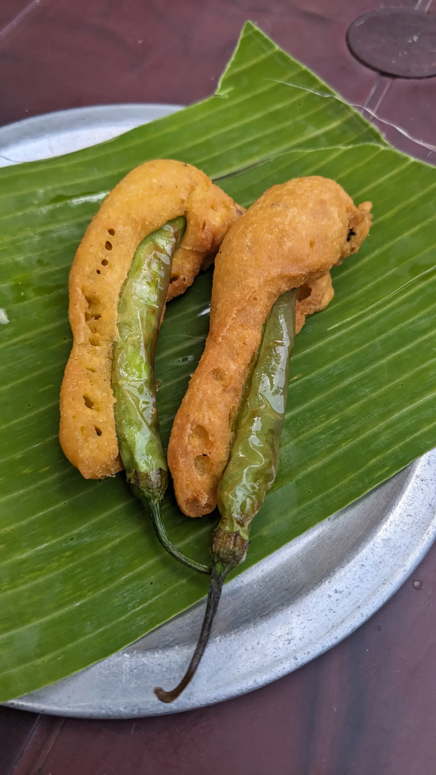 two long green chillies with a thick crispy batter on a banana leaf plate - mirchi bhaji